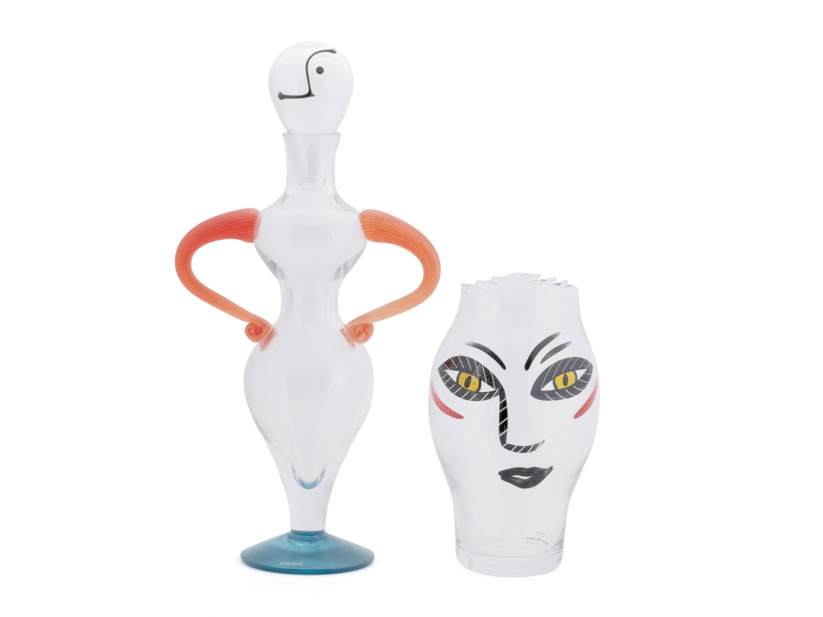 TWO PIECES OF KOSTA BODA FIGURAL ART GLASS: TWO PIECES OF KOSTA BODA FIGURAL ART GLASS Swedish, 20th century. A "Fenix" figural decanter by Kjell Engman with clear glass body, blue base, orange handles, and a head form stopper on top. Together