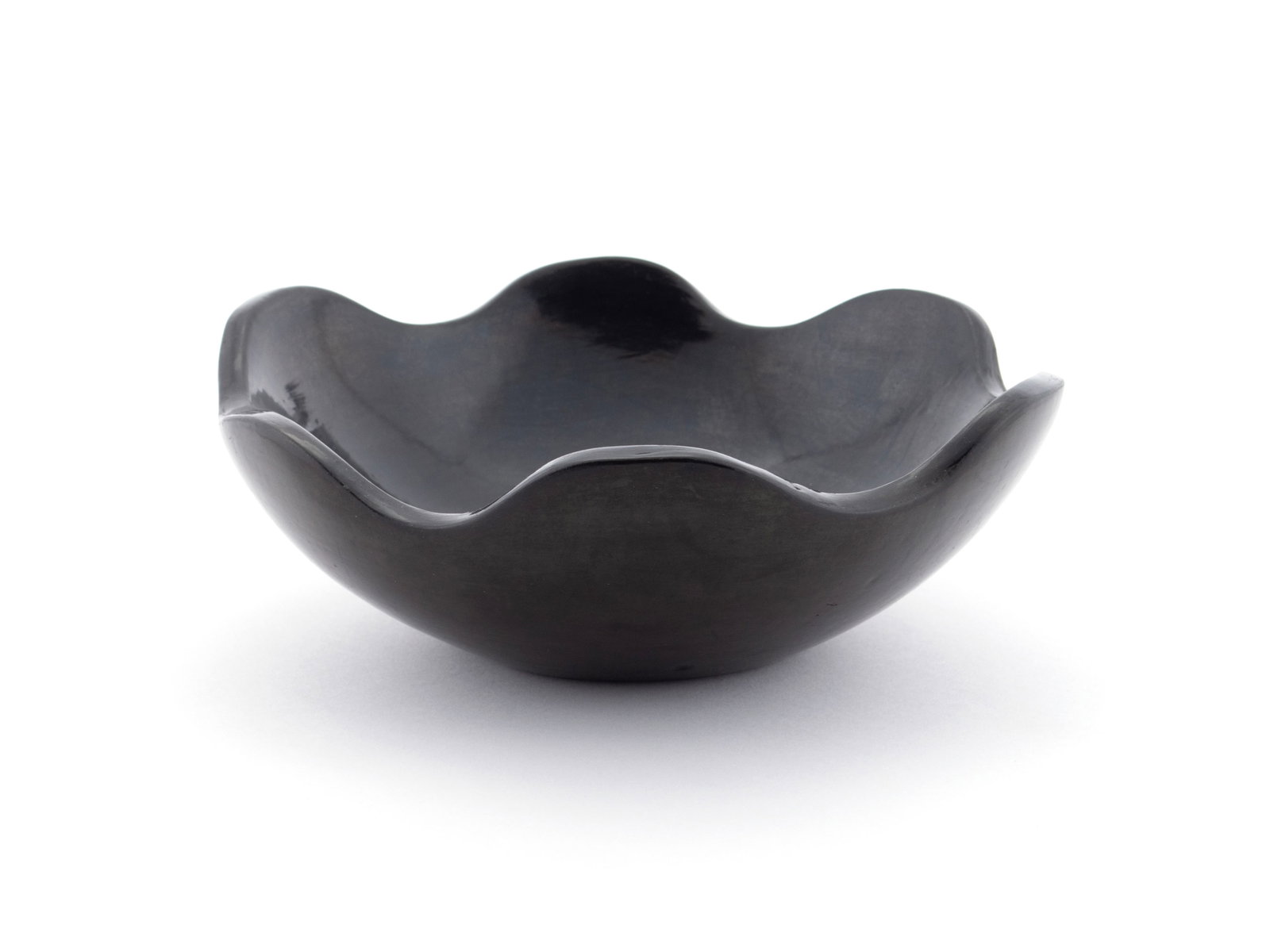 TONY AND JUANITA PENA BLACKWARE BOWL: TONY AND JUANITA PENA BLACKWARE BOWL San Ildefonso Pueblo, mid 20th century. Scalloped edge shallow bowl, signed on underside. 3 x 7 1/2 in. (7.6 x 19.1 cm.)