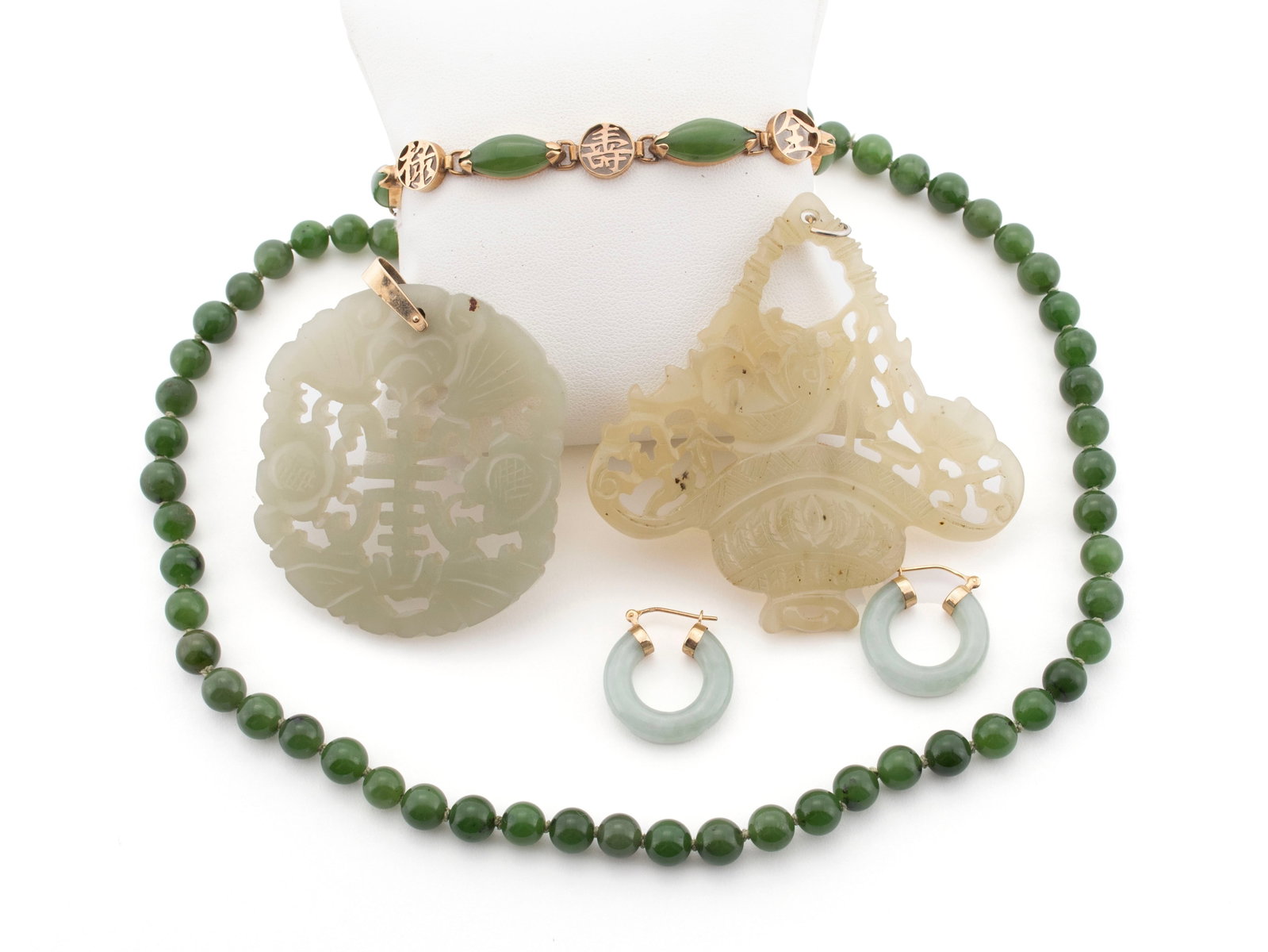 JADEITE JEWELRY GROUP: JADEITE JEWELRY GROUP One apple green beaded necklace, two carved pierced pendants, one 14k, jade and character link bracelet, and one pair of 10k jade hoop earrings. Necklace: 16 in. (40.6 cm.),