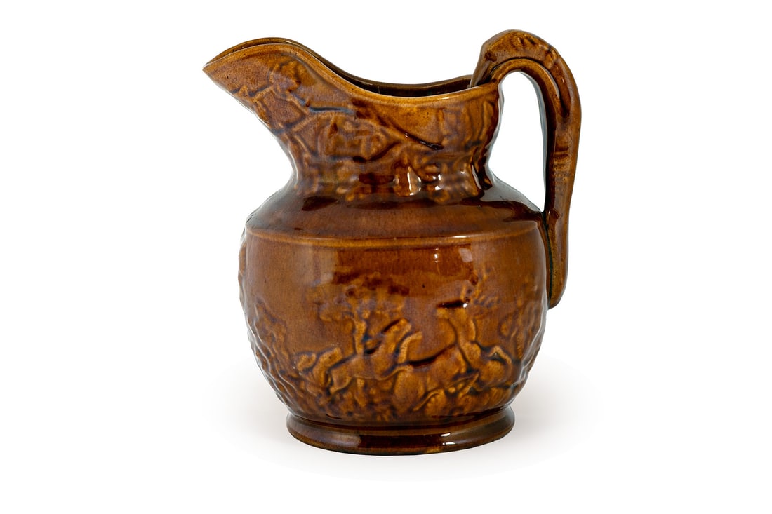 ROCKINGHAM GLAZE HUNT PITCHER: ROCKINGHAM GLAZE HUNT PITCHER American, 19th century. Molded pitcher with a hound handle and hunt scene around the exterior, unmarked. 8 in. (20.3 cm.)