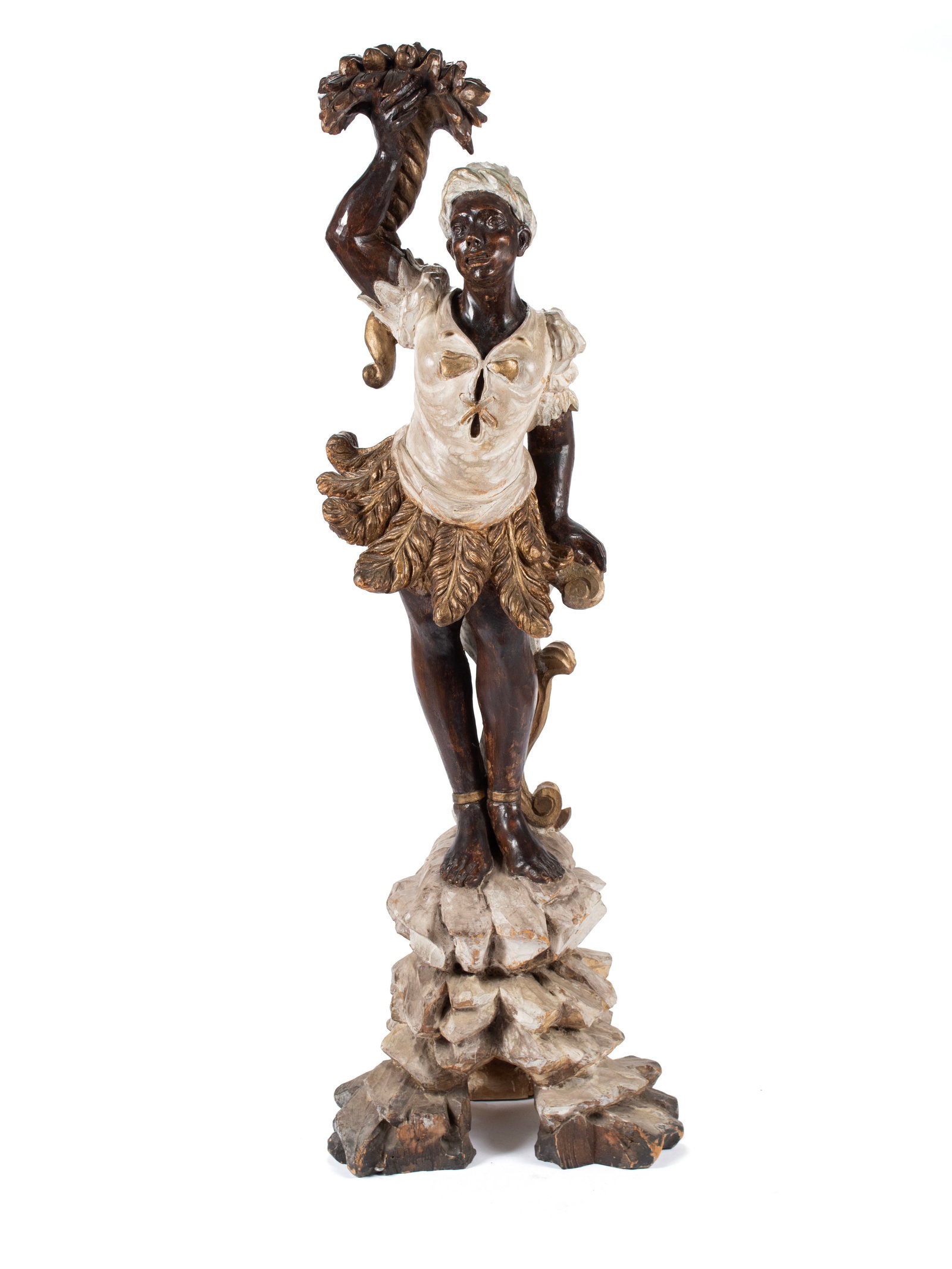 BLACKAMOOR FIGURAL CARVING: BLACKAMOOR FIGURAL CARVING Continental, 20th century, carved wood. Venetian style figure of a woman wearing a foliate skirt holding a spiraling cornucopia above her head, on a naturalistic rocky