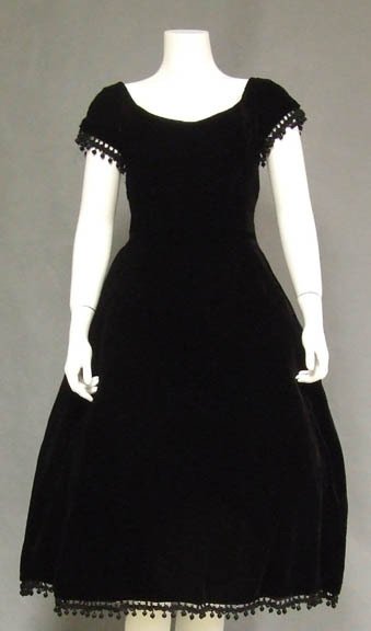 Harvey Berin Rich Black Velvet 1950: An elegant 1950s cocktail dress in a rich black velvet. Sleeves and hem are accented with thick braid, jet beads, and silk ball trim. Short sleeved fit and flare dress with scooped neckline. Dress has