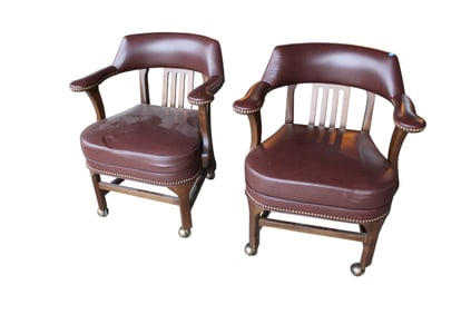 Pair of leather like arm chairs on rollers in a walnut frame