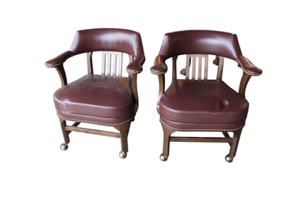 Pair of leather like arm chairs on rollers in a walnut frame