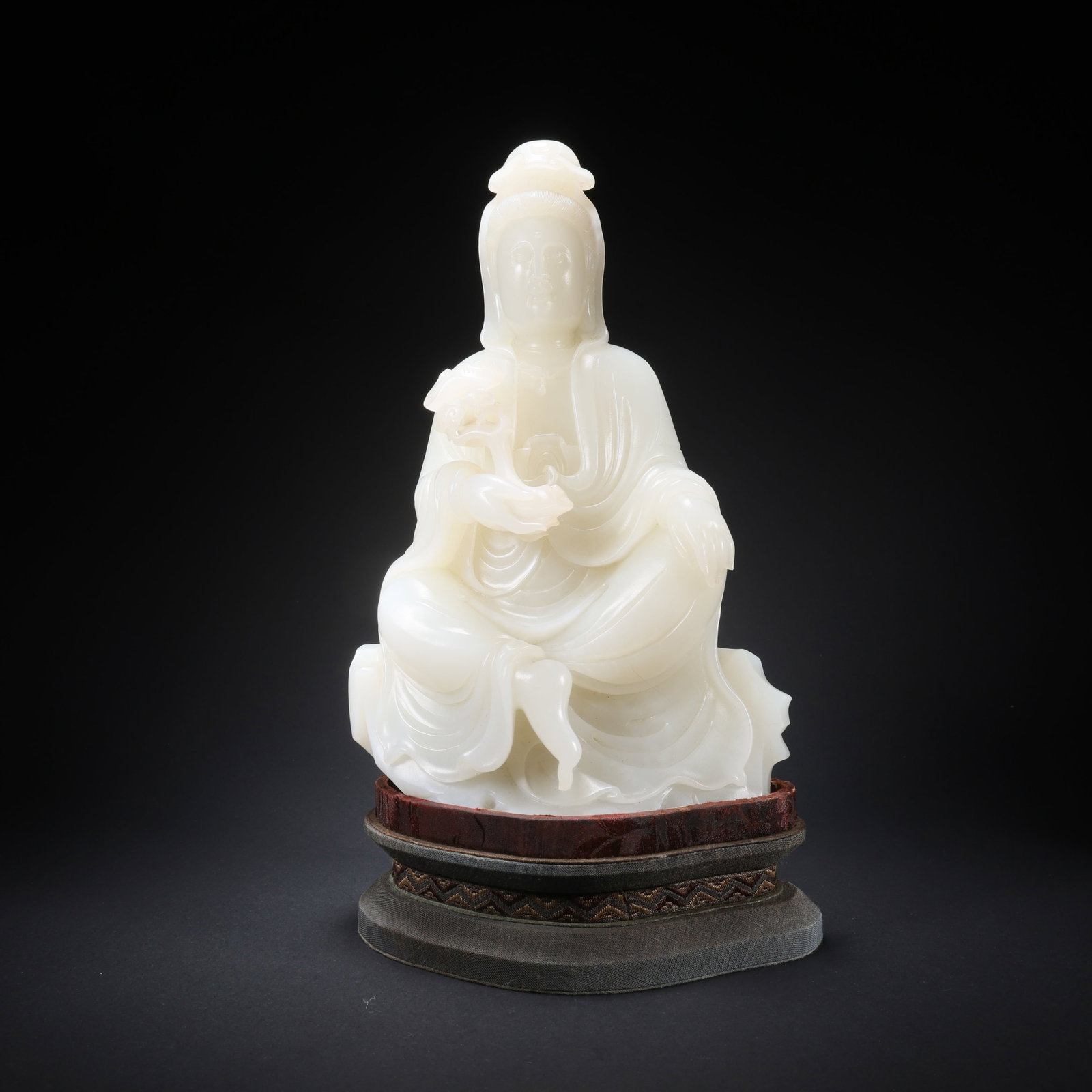 A seated Guanyin holding a ruyi scepter on a Qing Dynasty Hetian jade stand.: H. 26.3 cm. H. 22.6 cm. W. 15.1 cm.