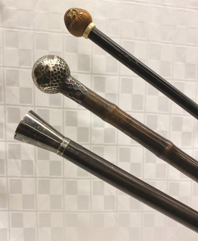 Three Canes: One Black Shaft with Japanese Netsuke Wood: Wood Face with Moveable Eyes, One Round Dimpled Wood (sterling) on a Bamboo Shaft, and One Sterling Tapered Top with Trick Opening for taking Snuff Condition: All good