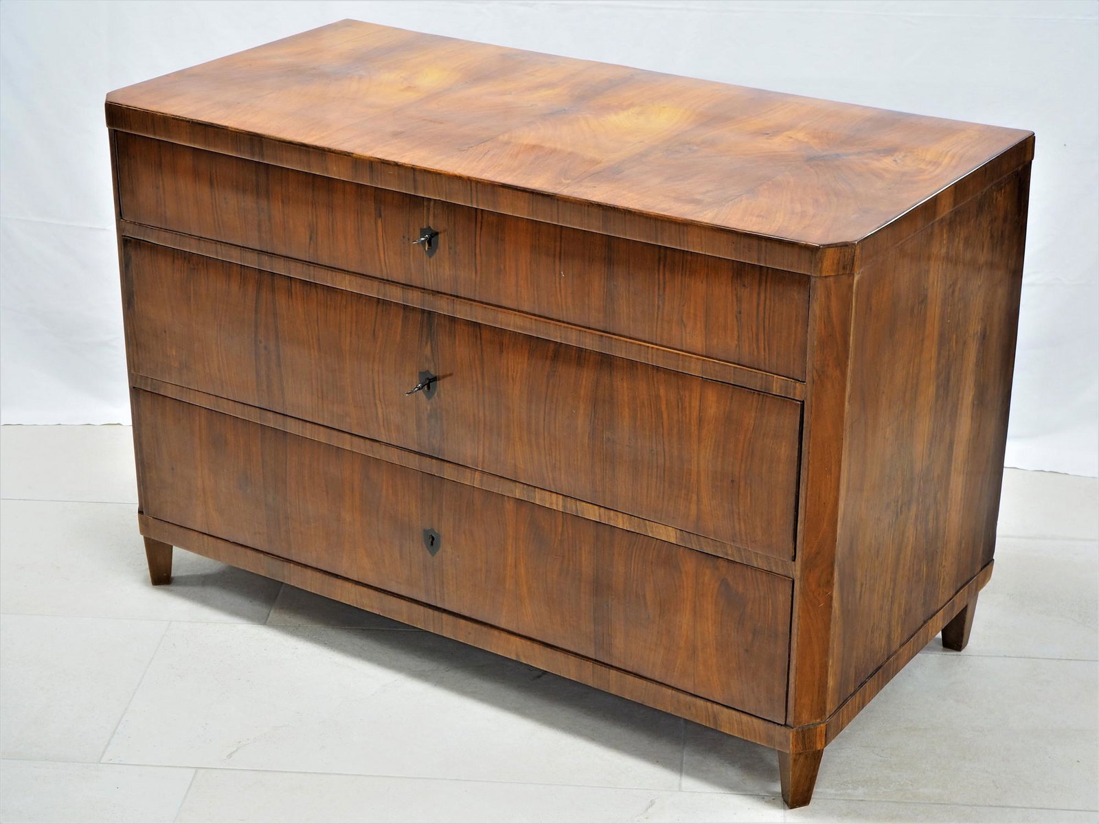 Biedermeier chest of drawers around 1820: Biedermeier chest of drawers around 1820 Body made of coniferous wood, veneered with walnut. Very nice grain. Straight form with beveled corners. Tapered pointed feet. Three lockable drawers, original