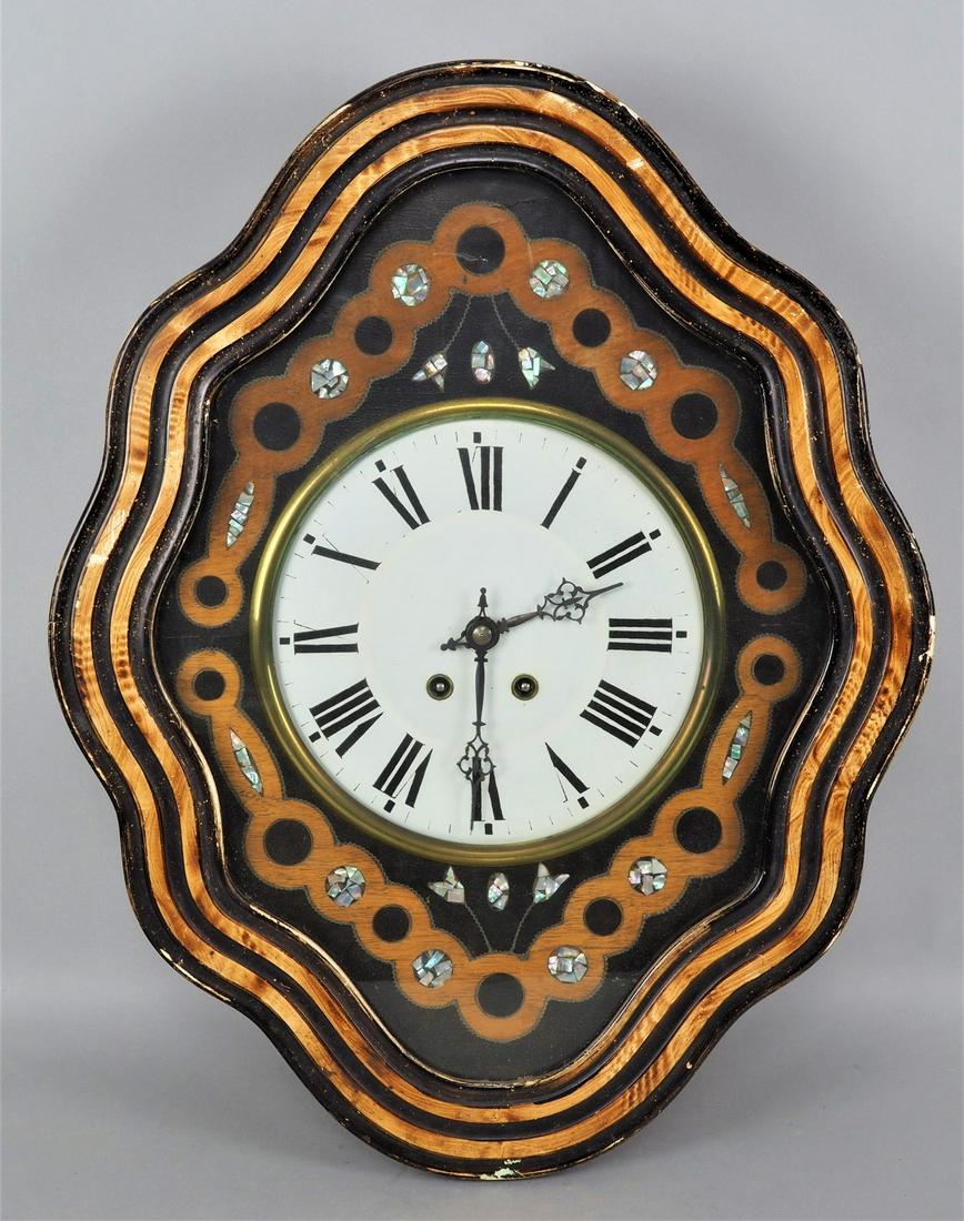 Wall clock "Ox eye": Wall clock "Ox eye" Wooden case, partly blackened, oval wavy shape. Front frame folds up, large white dial with Roman numerals. Blackened steel hands, built-in brass plate movement with strike on the