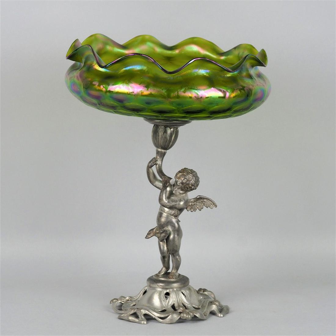 Art Nouveau fruit bowl, around 1900: Art Nouveau fruit bowl, around 1900Wide openwork stand decorated with floral motifs, standing on it winged putto, holding a flower in his hands, in it fixed glass bowl by "Loetz", strongly bulged, wav