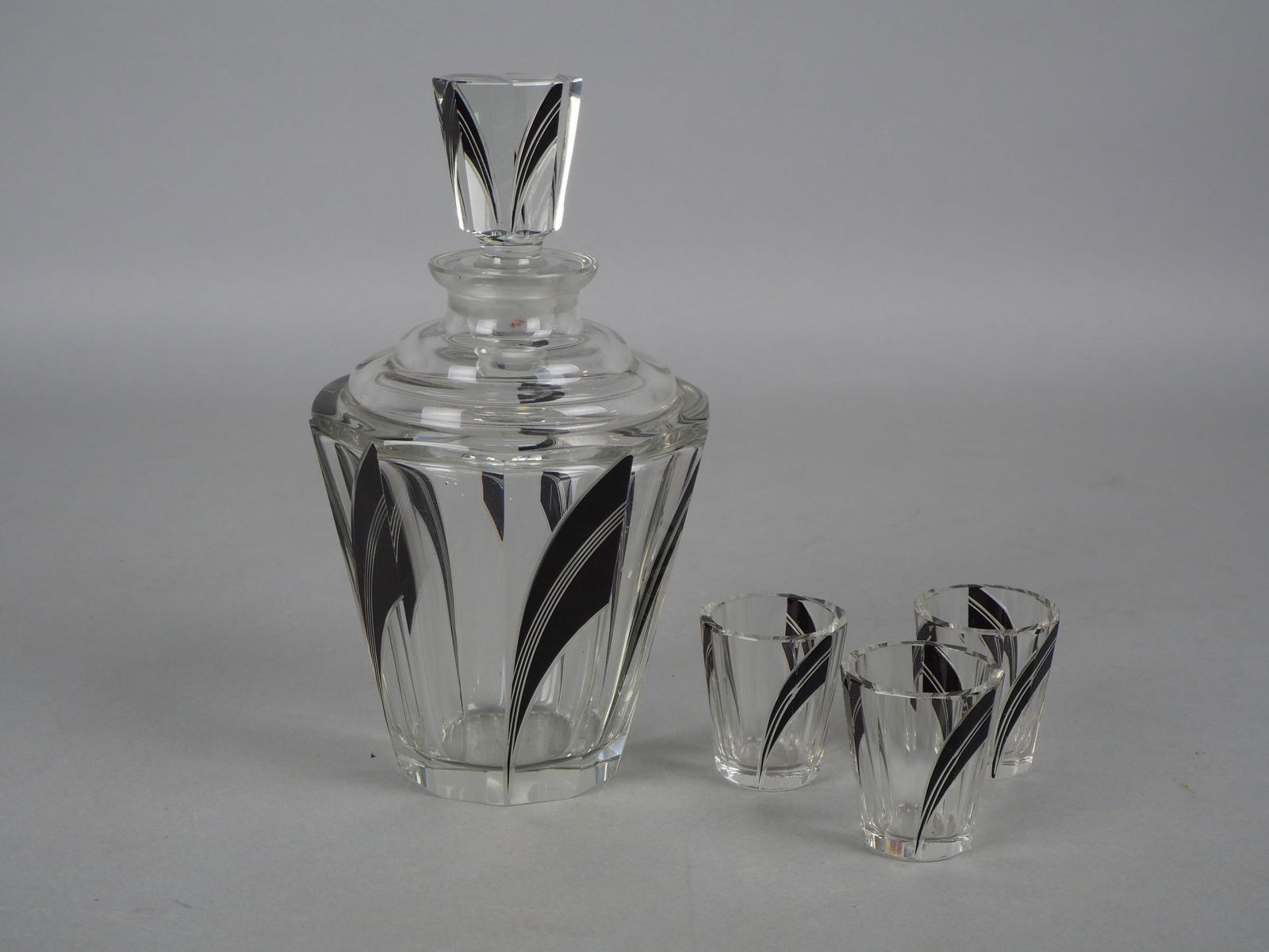 Art Deco liqueur set, c. 1920 - Karel Palda: Art Deco liqueur set, c. 1920 - Karel PaldaMade of heavy transparent crystal glass with cut decor and facets, with integrated black decor. Consisting of a carafe with large stopper and three stamps, v