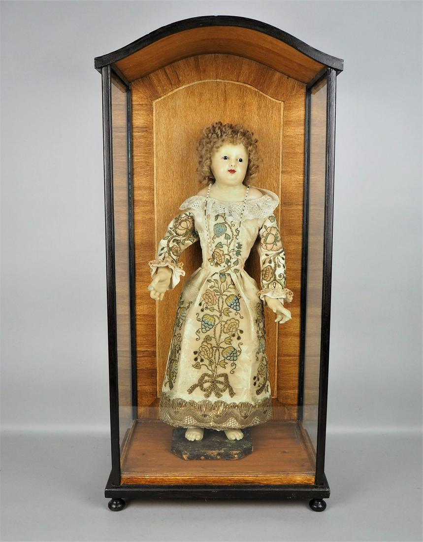 Wax doll with brocade robe in showcase around 1900.: Wax doll with brocade robe in showcase around 1900.Large wax doll in a wooden showcase (added later) with three glazed sides. Doll made of light wax with painted face and inset glass eyes, mounted on 