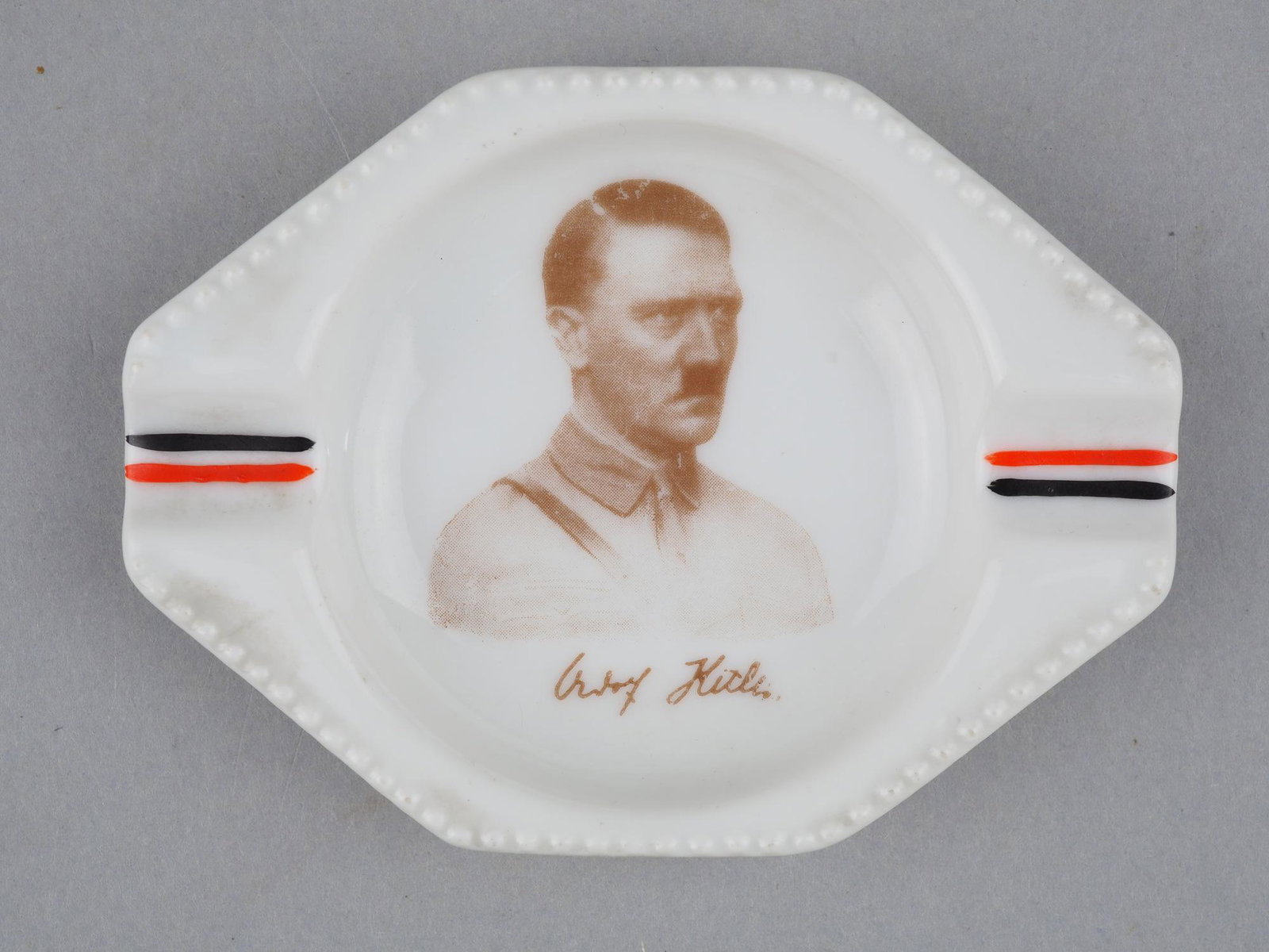 Adolf Hitler commemorative ashtray: Adolf Hitler commemorative ashtraysmall porcelain ashtray by Schumann Bavaria, stamped in blue on the back. Inside with portrait of A. Hitler in brown shirt. Deposit grooves painted with patriotic Rei