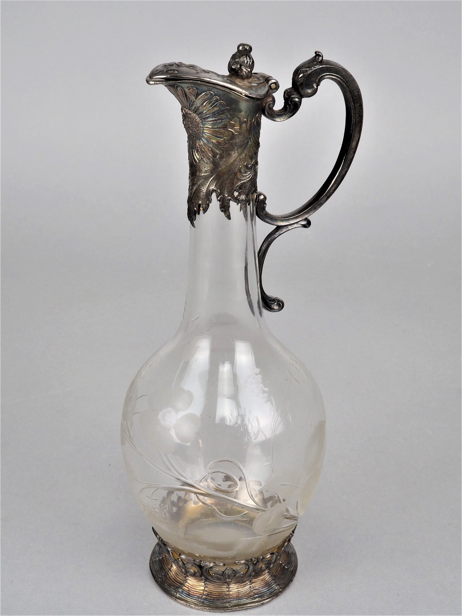 WMF carafe around 1900: WMF carafe around 1900made of light glass with floral cut decor. Basket-like stand made of metal, silver-plated. On the bottom company sign WMF ostrich mark and "as". Spout with lid and handle, also m