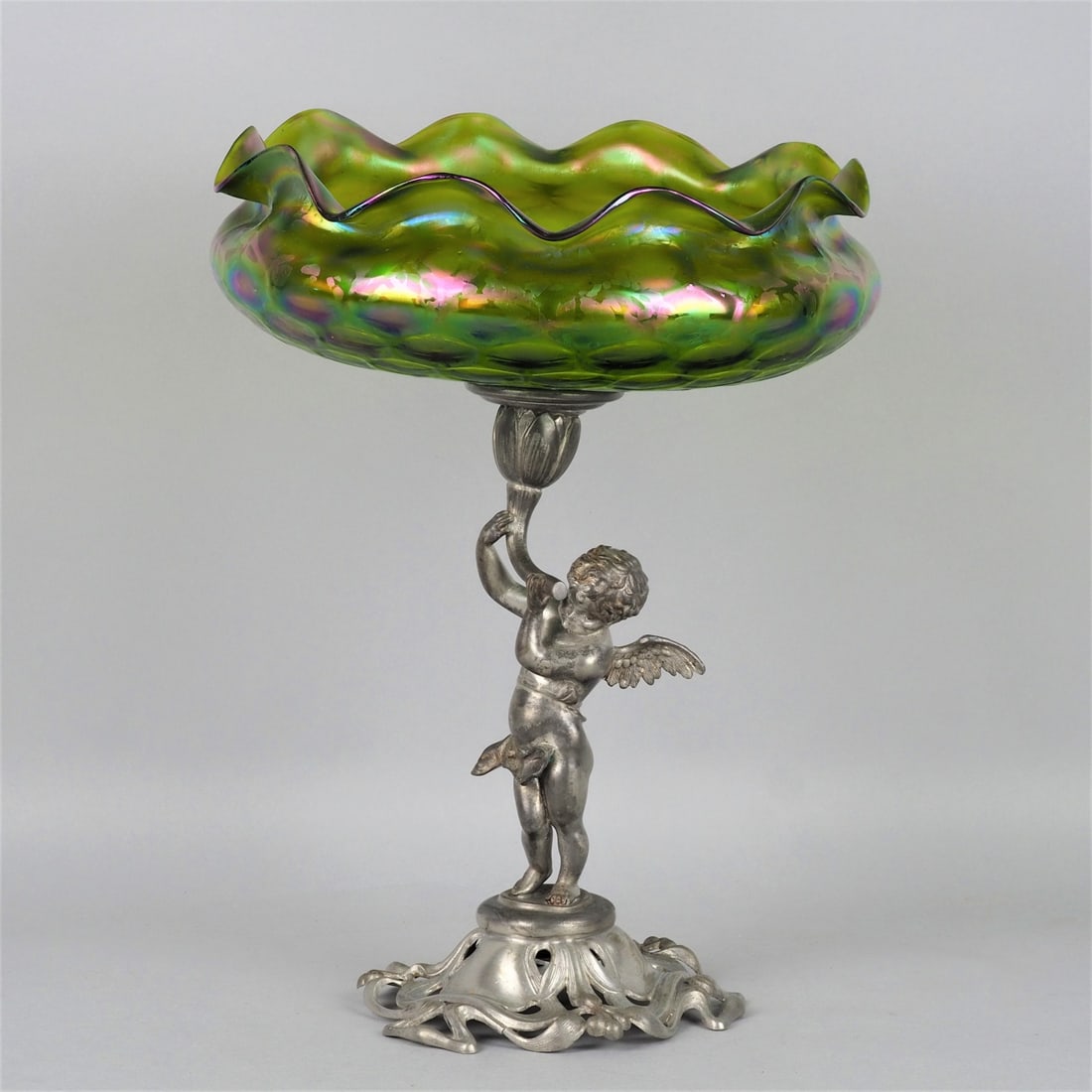Art Nouveau fruit bowl, around 1900: Art Nouveau fruit bowl, around 1900Wide openwork stand decorated with floral motifs, standing on it winged putto, holding a flower in his hands, in it fixed glass bowl by "Loetz", strongly bulged, wav