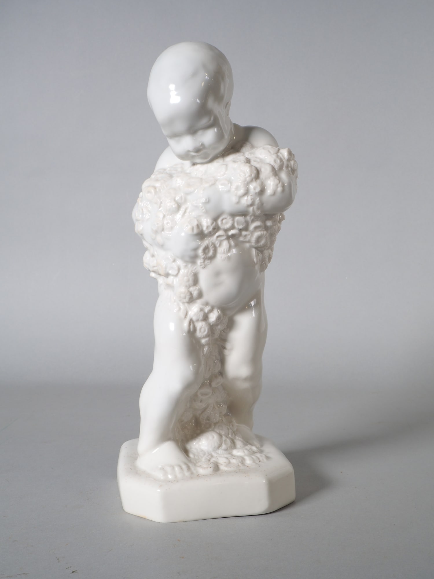 Art Nouveau porcelain figurine - seasonal putti ‘Spring’: Art Nouveau porcelain figurine - seasonal putti ‘Spring’Light-coloured body, glazed white, with pressed mark ‘LWY’ with crown on the back of the base. With firing crack in the floral arrangeme