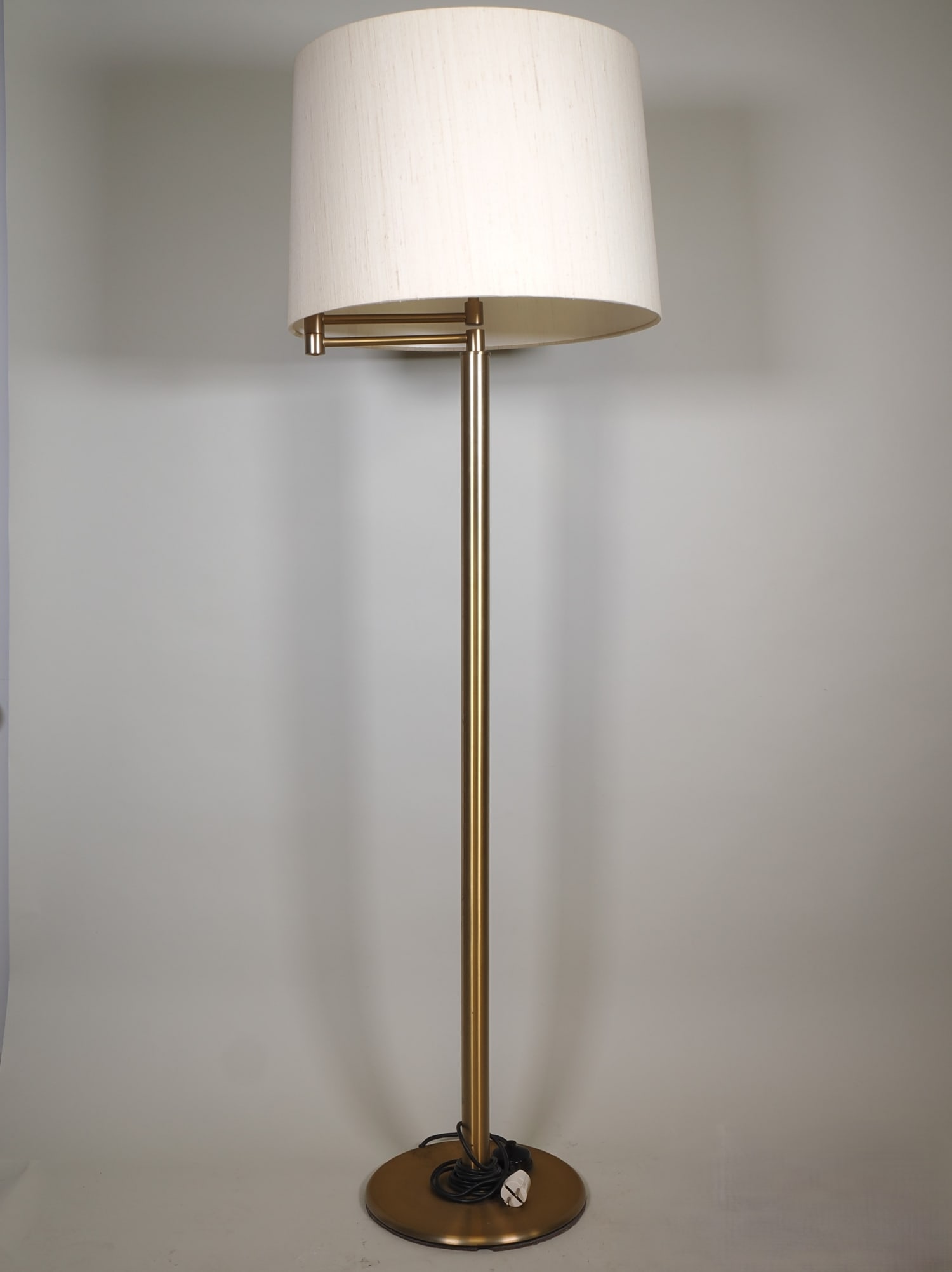Tall, swivelling brass floor lamp, mid-century: Tall, swivelling brass floor lamp, mid-centuryBrass floor lamp on a round stand, cream-coloured, cylindrical fabric shade, mounted on a double swivel arm, three-light electrified. Hardly any signs of