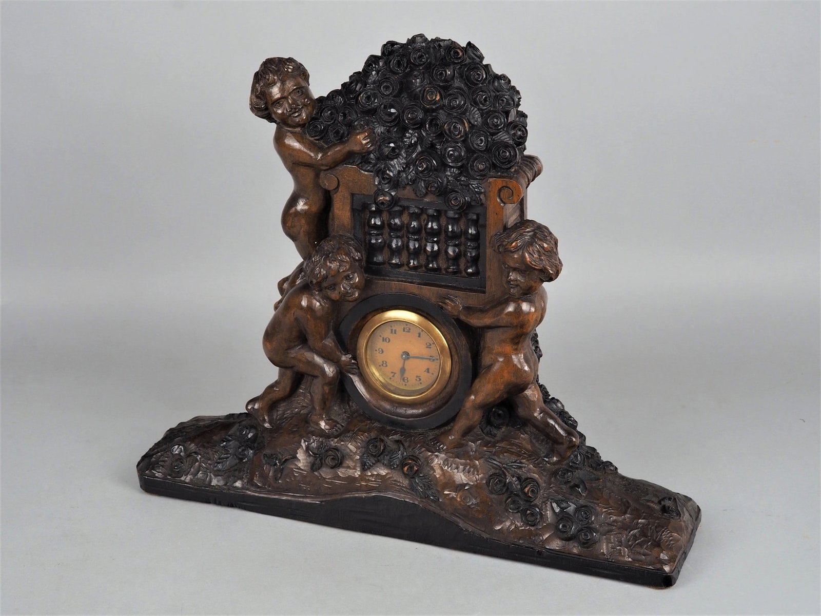 Leonhardt 1927, carver: Leonhardt 1927, carverMasterfully carved clock case in walnut wood, rectangular wide stand, standing puttos on it, in between built in movement with brass frame and glazed dial, on the back clock hand