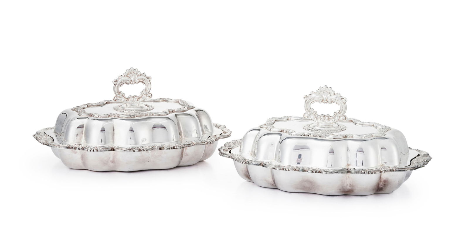 Paire de légumiers polylobés en métal argenté, XXe s., à décor de volu: Paire de légumiers polylobés en métal argenté, XXe s., à décor de volutes et feuillage, couvercle avec prise amovible formant jatte, long. 32 cm Provenance: Château