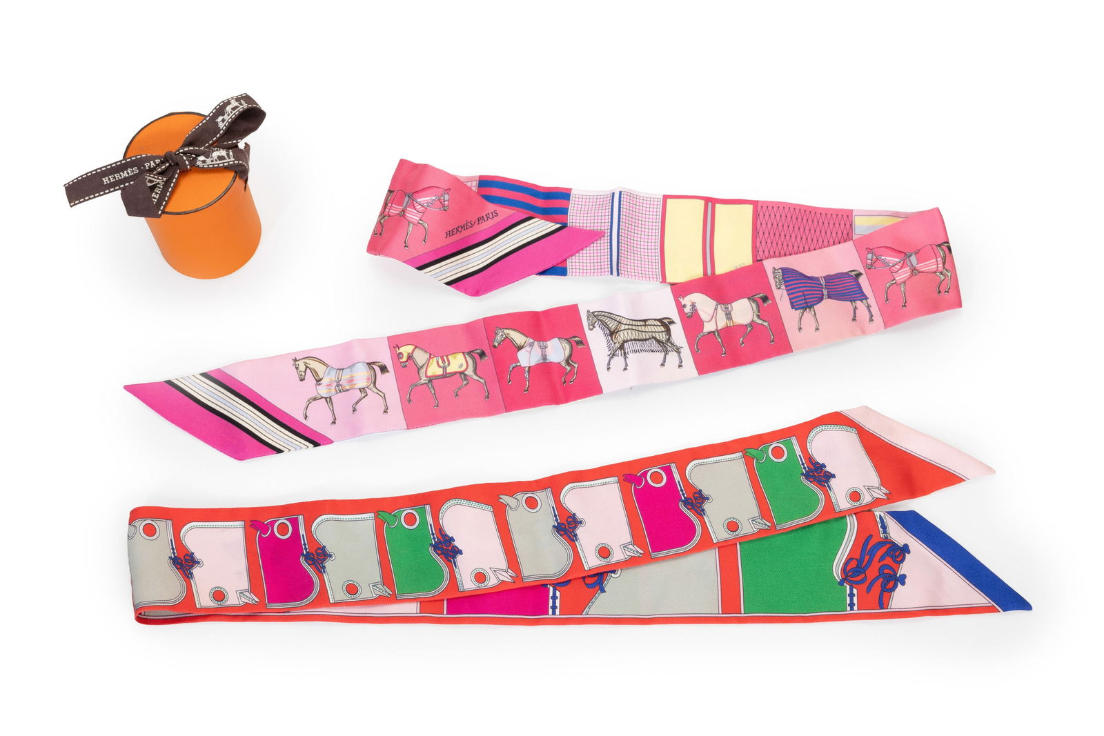 Hermès, 2 Twillys en twill de soie imprimé de motifs équestres, 1 boîte, 86,5x5 : Hermès, 2 Twillys en twill de soie imprimé de motifs équestres, 1 boîte, 86,5x5 cm Condition1 petit fil tiré sur le devant à la capuche grise 