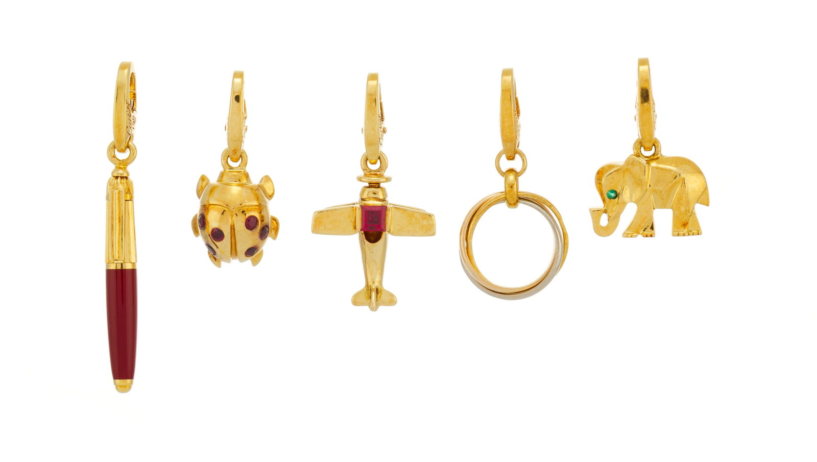 Cartier, lot de 5 charms or 750 comprenant un éléphant serti d'une émeraude, une cocc: Cartier, lot de 5 charms or 750 comprenant un éléphant serti d'une émeraude, une coccinelle et un avion sertis de rubis, un stylo Pasha en résine rouge et les anneaux Trinity, sign