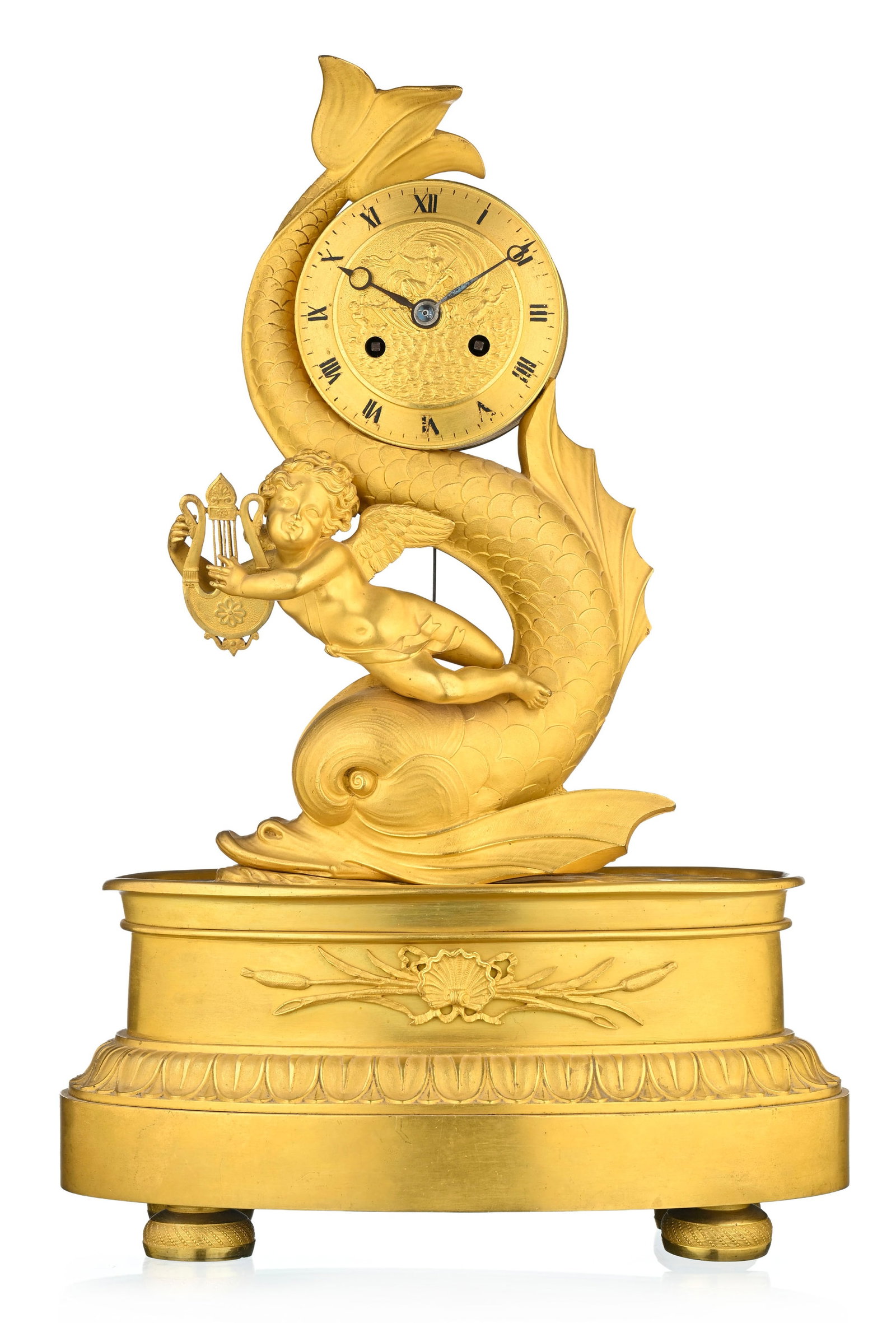 Pendule d'époque Restauration, en bronze doré et ciselé à décor d'un amour : Pendule d'époque Restauration, en bronze doré et ciselé à décor d'un amour tenant une lyre et reposant sur un dauphin, base ovale ornée de feuilles d'eau, 40x27x15 cm