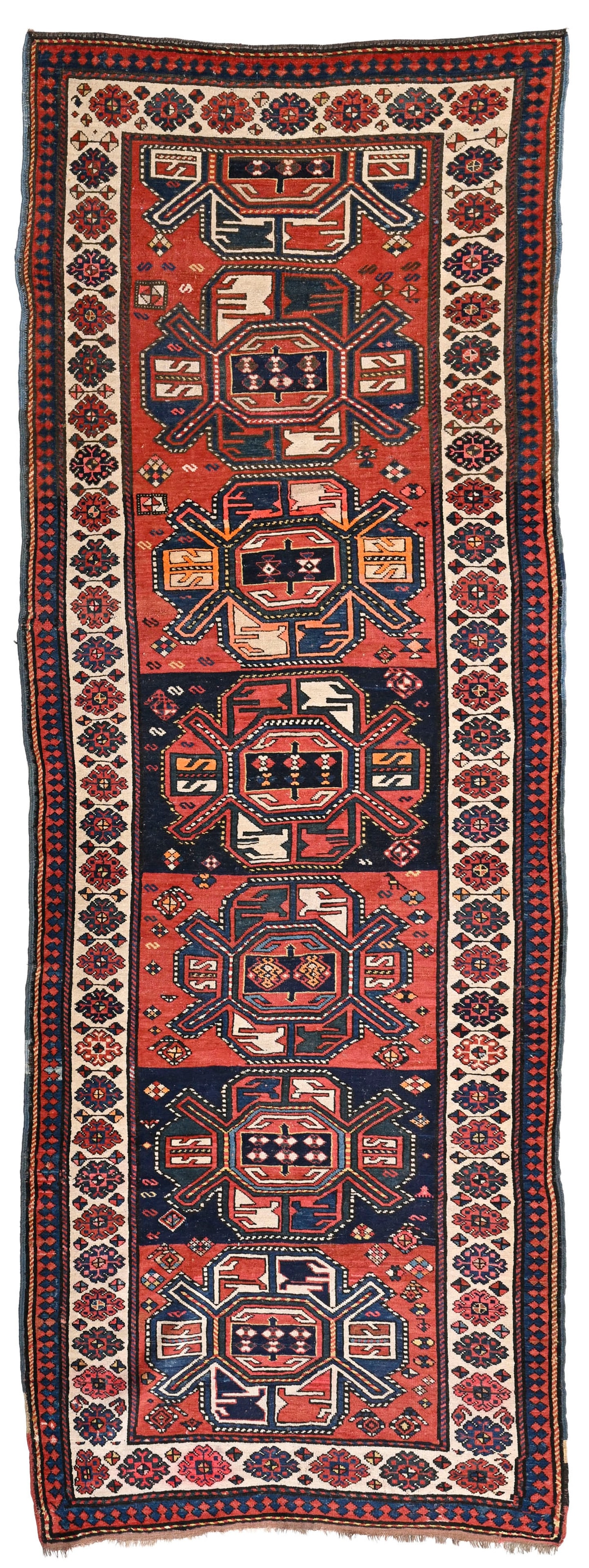 Tapis Kazakh, Caucase, 2ème tiers du XXe s., orné d'une rangée centrale de médai: Tapis Kazakh, Caucase, 2ème tiers du XXe s., orné d'une rangée centrale de médaillons polychromes sur fond rouge et bleu parsemé de fleurs stylisées, bordure beige