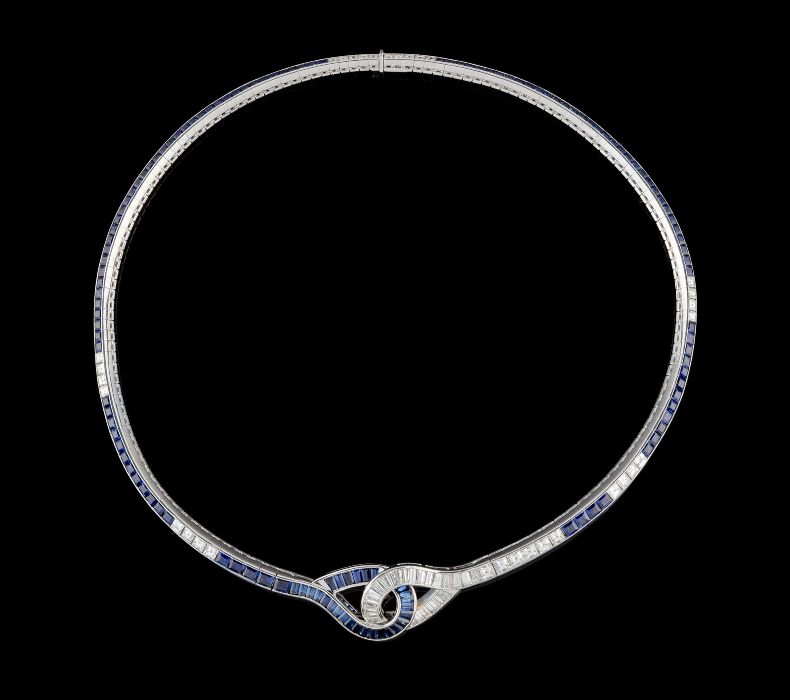 Gübelin, collier or gris 750 serti en ligne de saphirs et de diamants taille carré reli: Gübelin, collier or gris 750 serti en ligne de saphirs et de diamants taille carré reliée au centre en boucles entrelacées serties de saphirs et de diamants taille baguette et