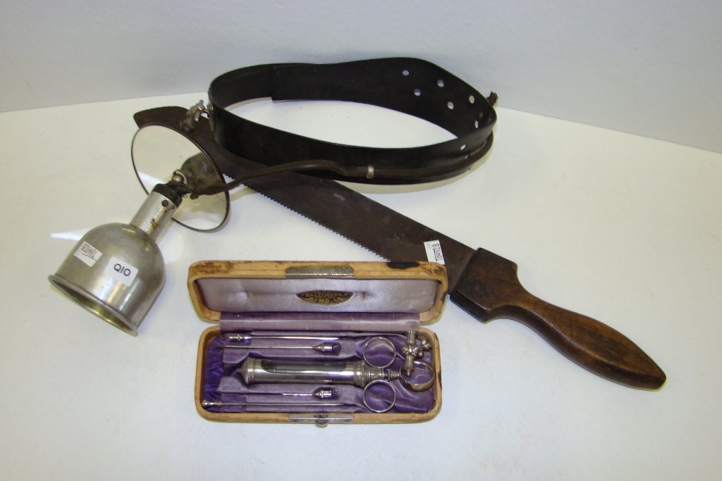 A group of vintage medical items, including amputa: amputation saw, aspirating syringe and head reflector with attached lamp