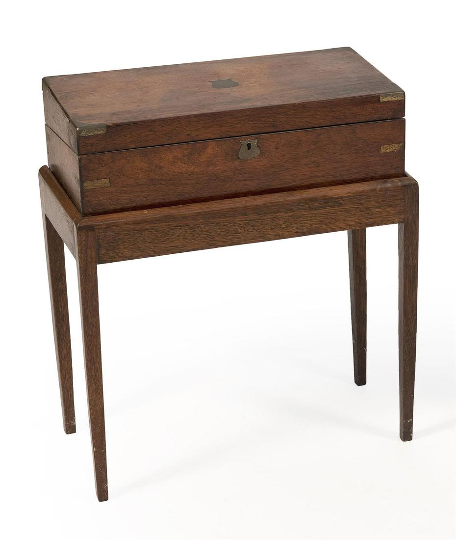 BRASS-BOUND LAP DESK ON STAND In walnut veneer. Brass: BRASS-BOUND LAP DESK ON STAND 19th Century In walnut veneer. Brass shield-form escutcheon and inlaid plaque. Contemporary stand fitted with a swing leg to support desk when opened. Total height 24". W