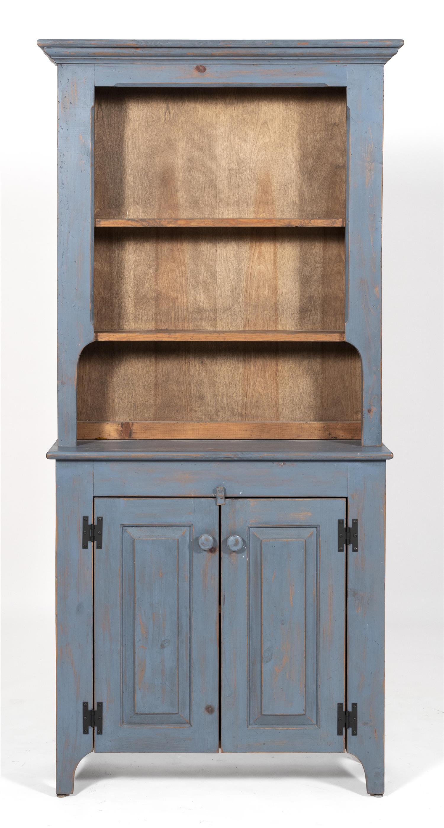 STEP-BACK CUPBOARD In pine, under blue paint. Upper: STEP-BACK CUPBOARD 20th Century In pine, under blue paint. Upper section with shaped cornice and two shelves. Lower section with two paneled doors enclosing one interior shelf. Height 70.25". Width 32