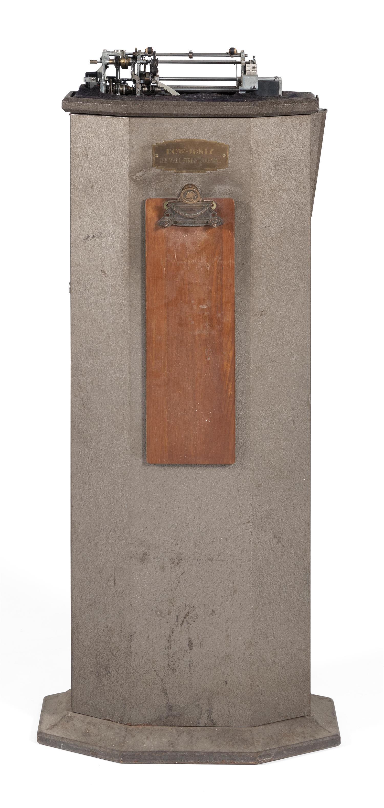 DOW JONES TICKER TAPE MACHINE Pot metal with a: DOW JONES TICKER TAPE MACHINE Pot metal with a brown-gold finish. Plaque mounted on front marked "Dow-Jones The Wall Street Journal". Similarly marked bronze and wood clipboard also attached to front.