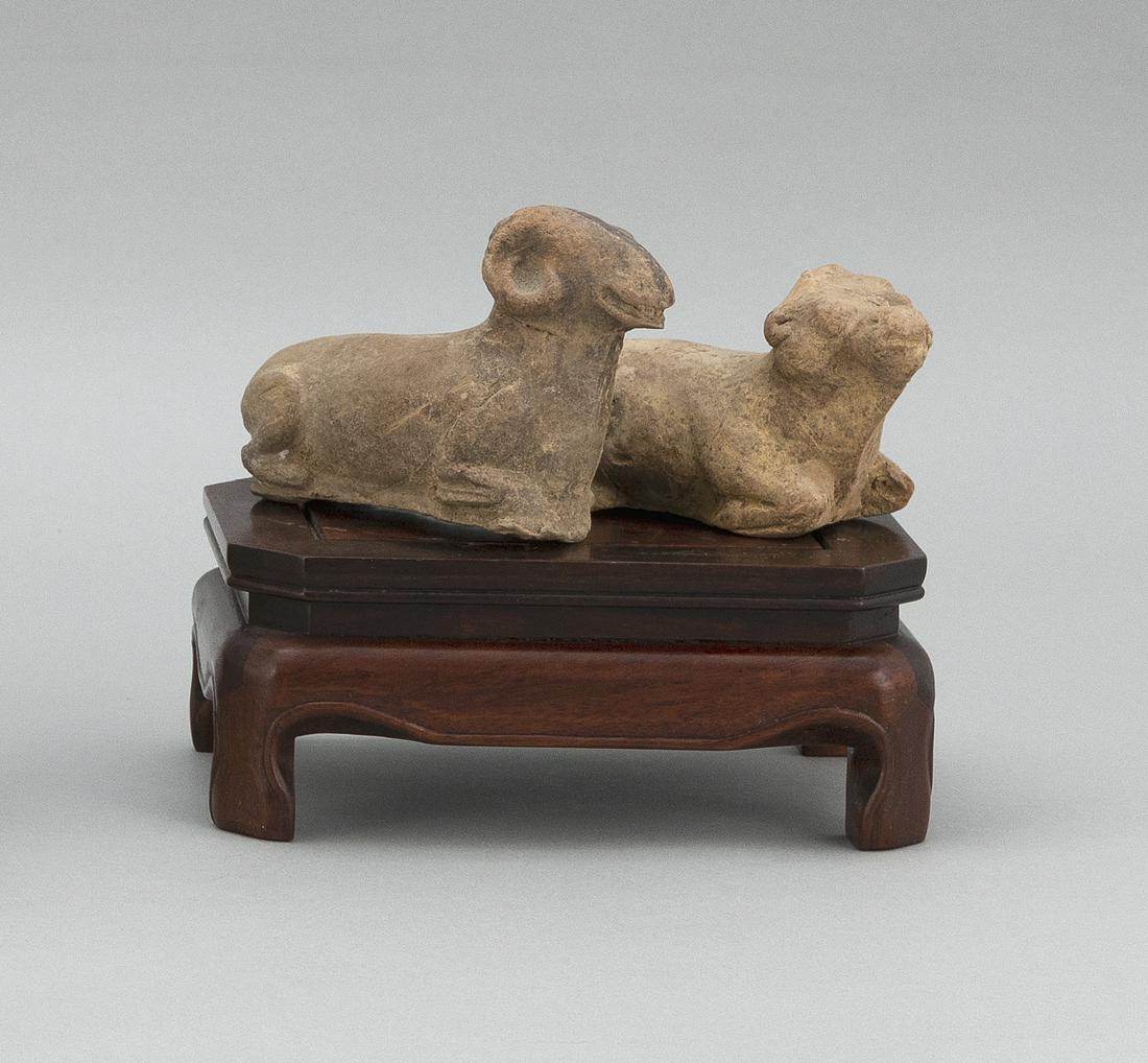 PAIR OF CHINESE POTTERY RECUMBENT RAMS Possibly Han: PAIR OF CHINESE POTTERY RECUMBENT RAMSPossibly Han DynastyLengths 5". With rosewood stand. Stand height 3". Length 6".
