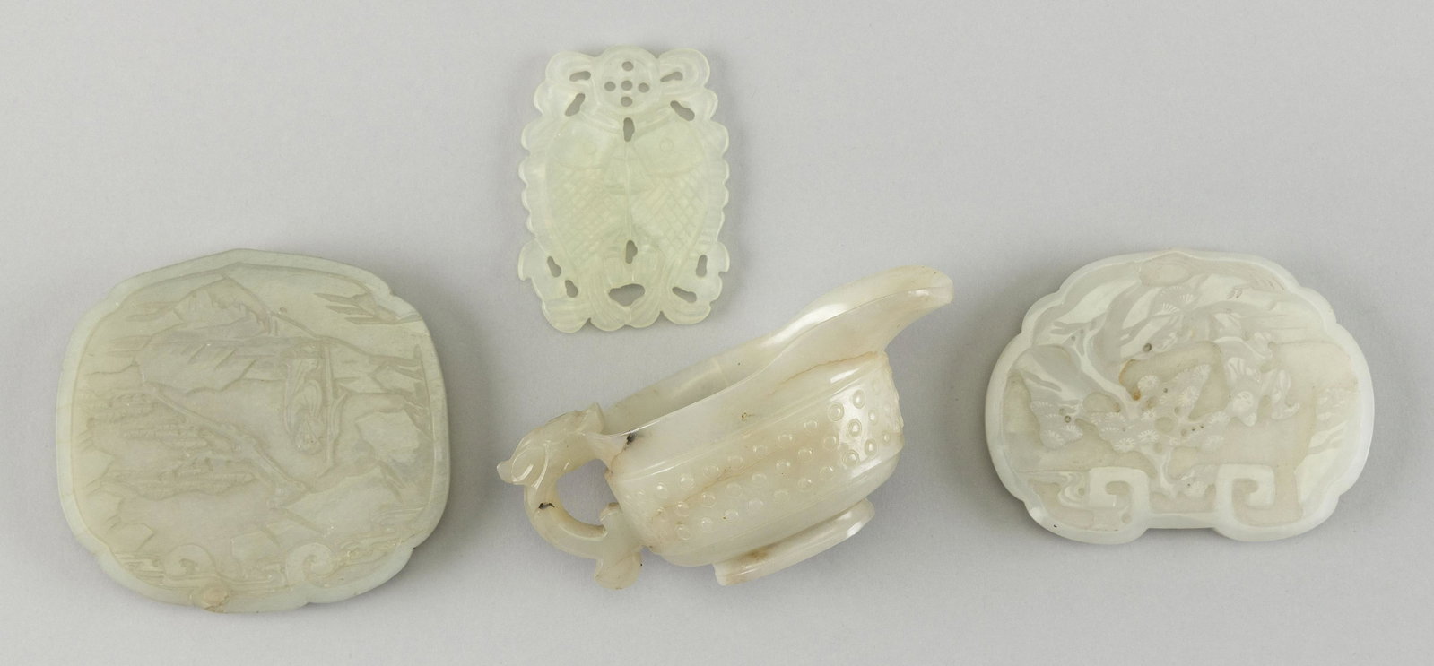 FOUR SMALL WHITE AND CELADON GREEN JADE AND JADEITE: FOUR SMALL WHITE AND CELADON GREEN JADE AND JADEITE OBJECTS 1) Double fish-form pendant. Length 2.5". 2-3) Two carved plaques, both with landscape and figural decoration. Lengths 3". 4) Wine