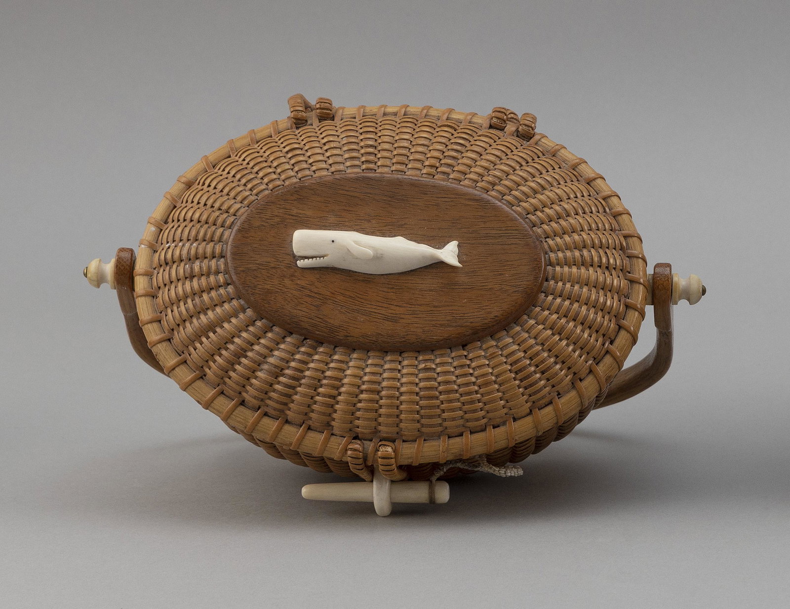 NANTUCKET BASKET PURSE BY STEPHEN GIBBS Nantucket,: NANTUCKET BASKET PURSE BY STEPHEN GIBBS Nantucket, Circa 1973 Oval, with swing handle. Carved sperm whale mounted to top of hinged lid. Presentation plaques mounted to interior of lid and base. Basket