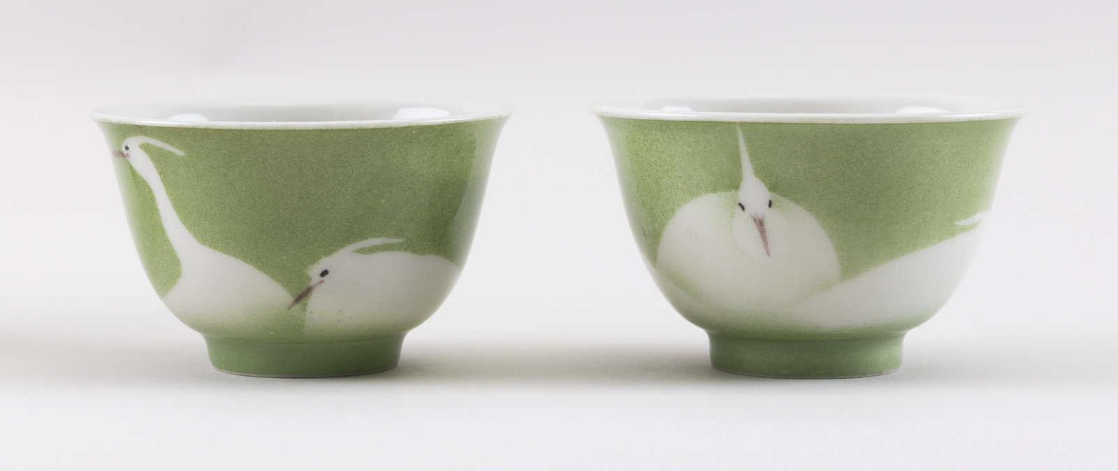 PAIR OF JAPANESE MAKUZU KOZAN PORCELAIN WINE CUPS 20th: PAIR OF JAPANESE MAKUZU KOZAN PORCELAIN WINE CUPS 20th Century In bell form on a slightly raised foot. Egret decoration on a celadon green ground. Signed on bases. Heights 2”. Diameters 3”.