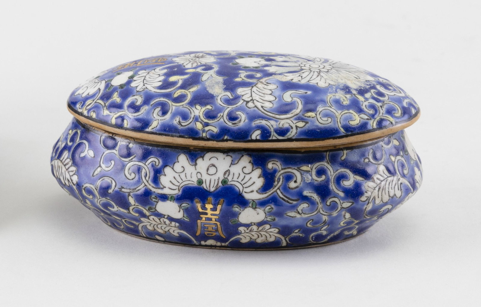 CHINESE BLUE AND WHITE PORCELAIN TRINKET BOX Early 20th: CHINESE BLUE AND WHITE PORCELAIN TRINKET BOX Early 20th Century Oval, with white enameled lotus, peach and bat decoration and green and gilt highlights on a cobalt blue ground. Red stamped mark on bas