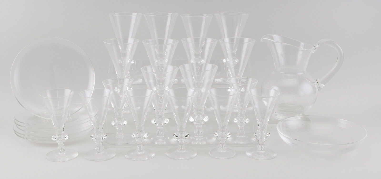 STEUBEN CRYSTAL PITCHER, BOWL, BARWARE AND PLATES: STEUBEN CRYSTAL PITCHER, BOWL, BARWARE AND PLATES SERVICEStemware pattern 7737. Includes a water pitcher, height 9", six plates, diameters 8", eight red wine goblets, diameters 6", ten