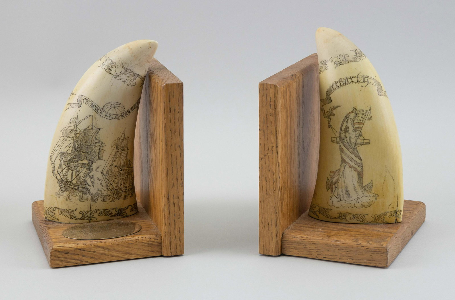 PAIR OF ARTEK ENGRAVED SIMULATED WHALE'S TEETH 20th: PAIR OF ARTEK ENGRAVED SIMULATED WHALE'S TEETH 20th Century Engraved with patriotic and naval engagement motifs. Mounted as bookends on oak bases. Heights 8”.