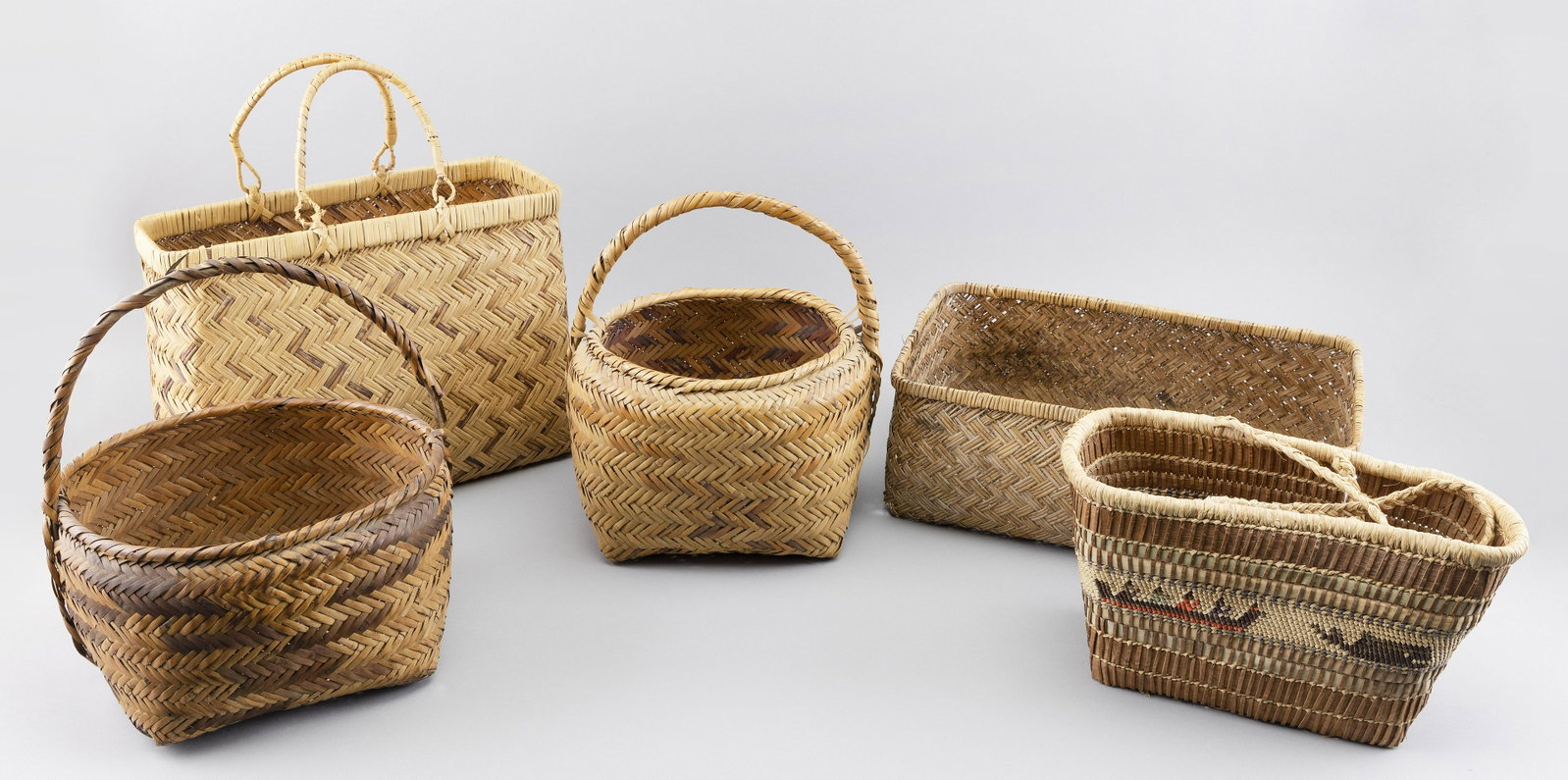 FIVE AMERICAN INDIAN BASKETS Mid- to Late 20th Century Lengths from 10.5" to 16”.: FIVE AMERICAN INDIAN BASKETS Mid- to Late 20th Century One handled example with central band of five-color decoration of fisherman, whale and eagle. Lengths from 10.5" to 16”.