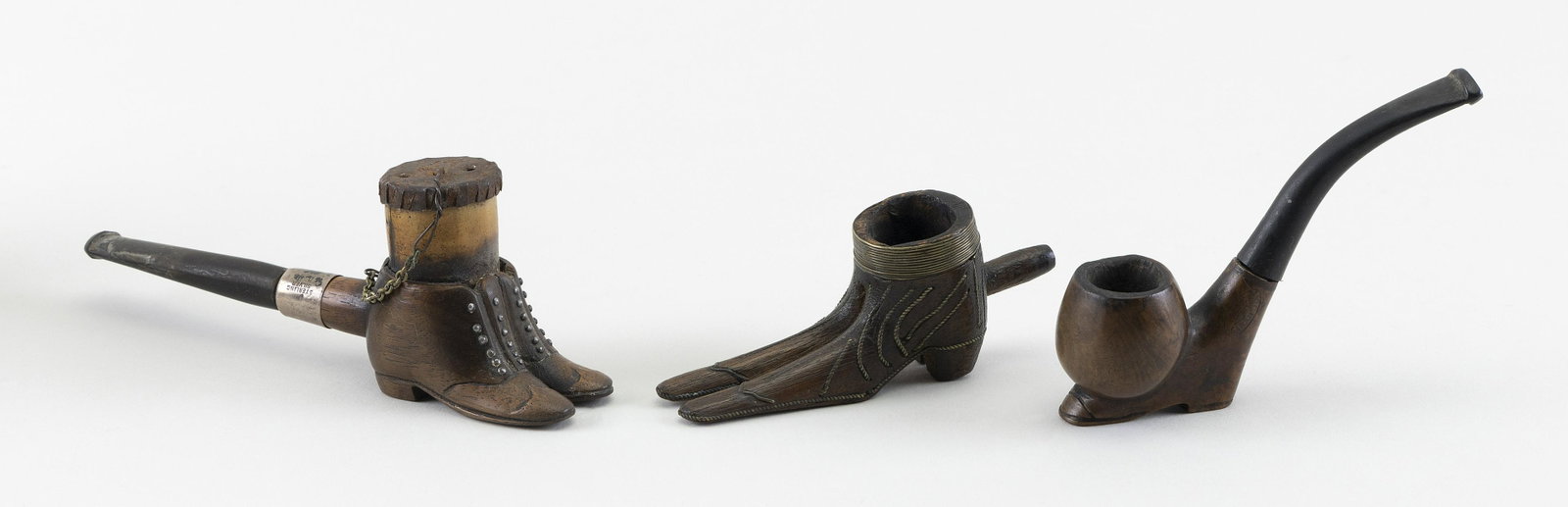 THREE BOOT-FORM TREEN PIPES Late 19th/Early 20th Century Lengths to 5.75”.: THREE BOOT-FORM TREEN PIPES Late 19th/Early 20th Century 1) A pair of boots with wire work inlay. 2) Impressed “Radica Garantita”. 3) Pair of boots with sterling silver collar. Lengths to 