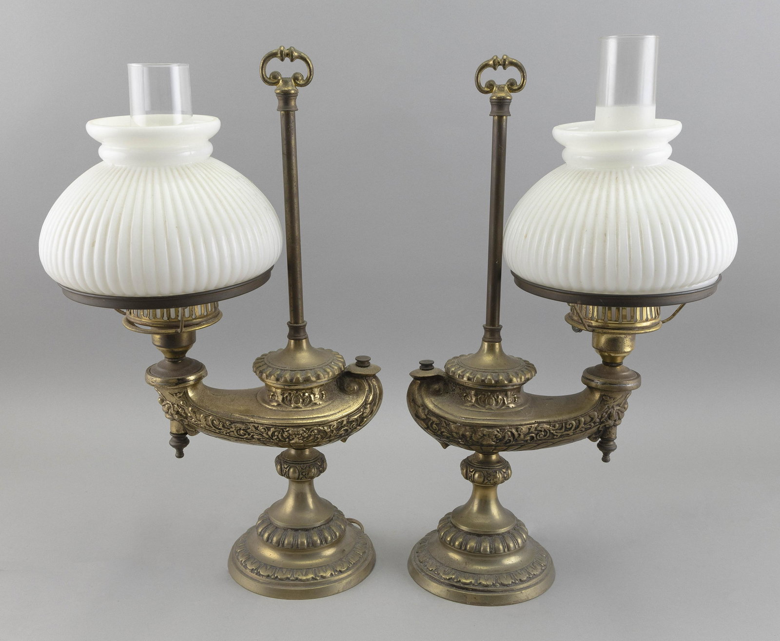 NEAR-PAIR OF HEAVY BRASS TABLE LAMPS Early 20th Century Heights 19.25”.: NEAR-PAIR OF HEAVY BRASS TABLE LAMPS Early 20th Century Aladdin form. Opaque white shades and frosted chimneys. Heights 19.25”.