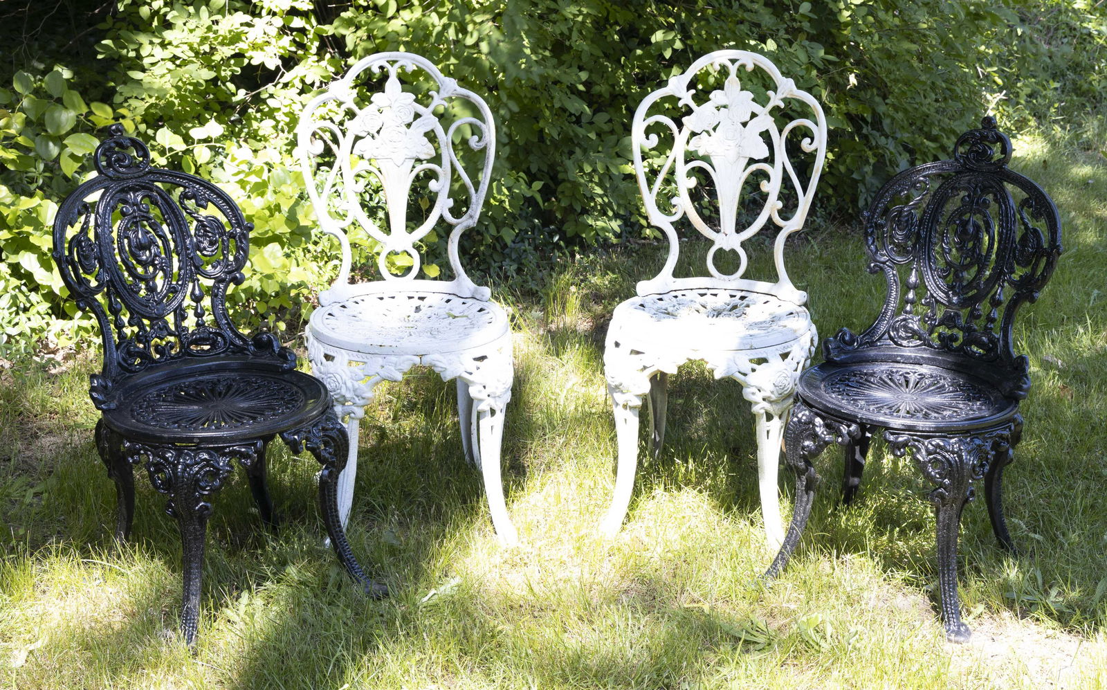 FOUR PAINTED CAST IRON GARDEN CHAIRS 20th Century Back heights 35” and 32”.: FOUR PAINTED CAST IRON GARDEN CHAIRS20th CenturyTwo white with floral design and two black with swag design.Back heights 35” and 32”.