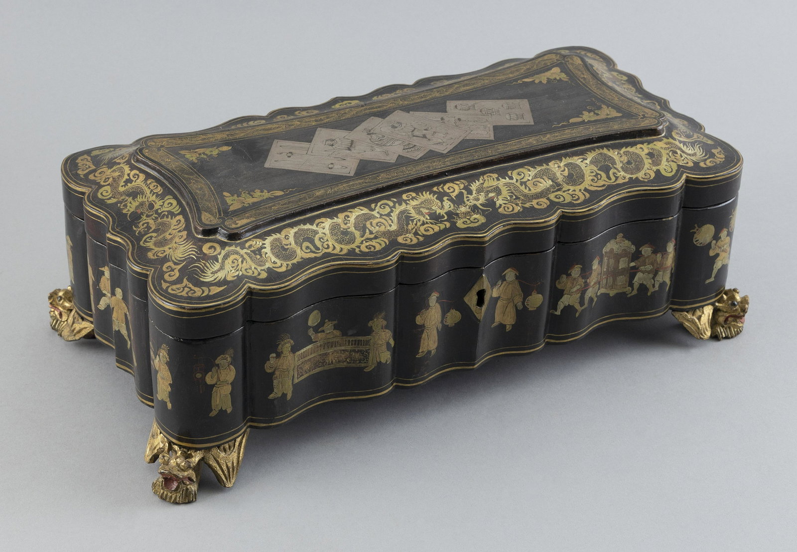 CHINESE POLYCHROME AND GILT-DECORATED BLACK LACQUER GAMES BOX Mid-19th Century Height 4.25". Length: CHINESE POLYCHROME AND GILT-DECORATED BLACK LACQUER GAMES BOX Mid-19th Century Hinged lid with dragon and cloud design around perimeter and a depiction of six game pieces at center. Shaped sides with 