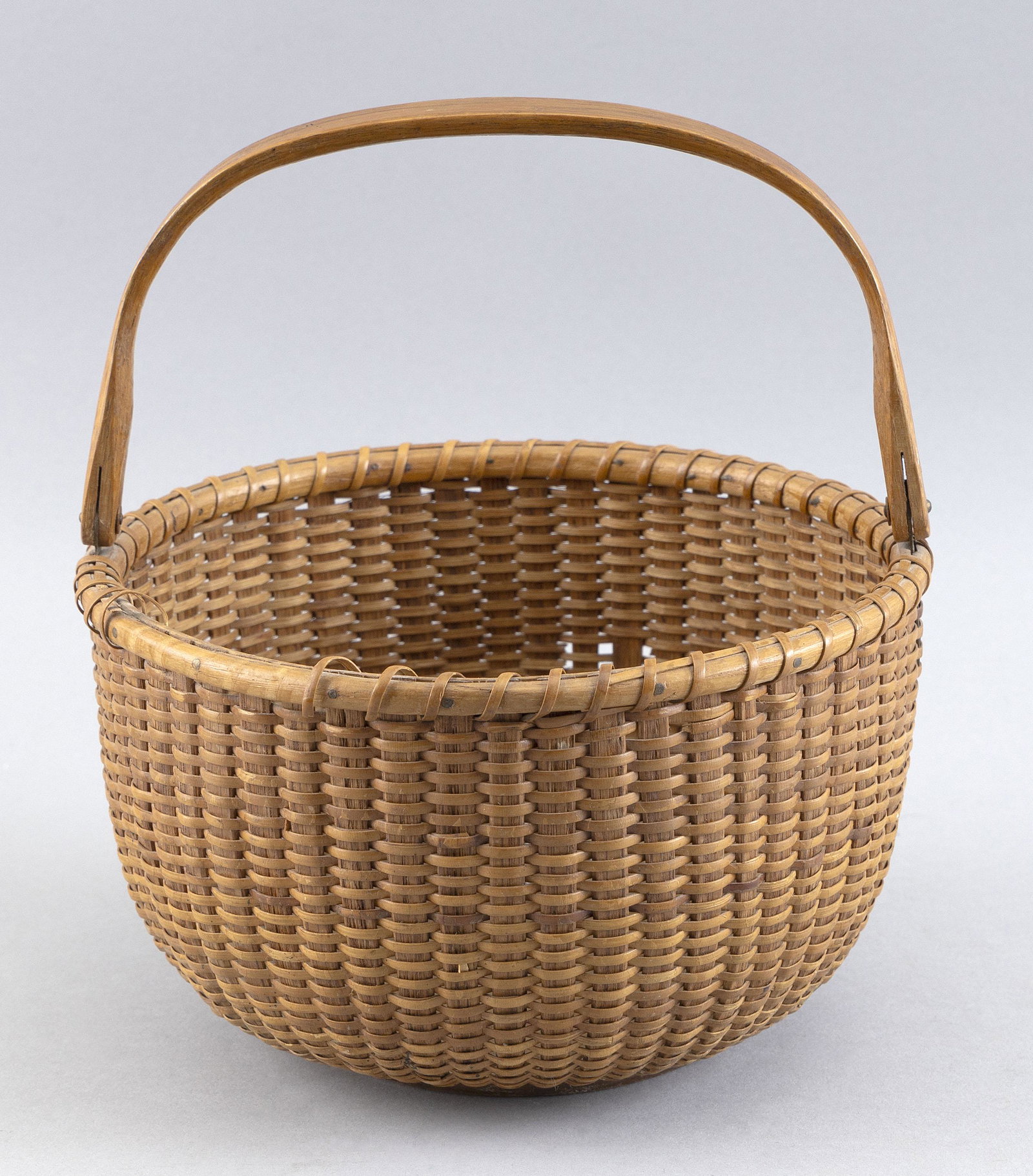 NANTUCKET BASKET Last Quarter of the 19th Century Height to rim 4.5". Diameter 7.5".: NANTUCKET BASKETLast Quarter of the 19th CenturyOak rim and staves and maple base plate. Oak swing handle attached with metal ears. Interior of base plate with two pairs of concentric incised rings.He