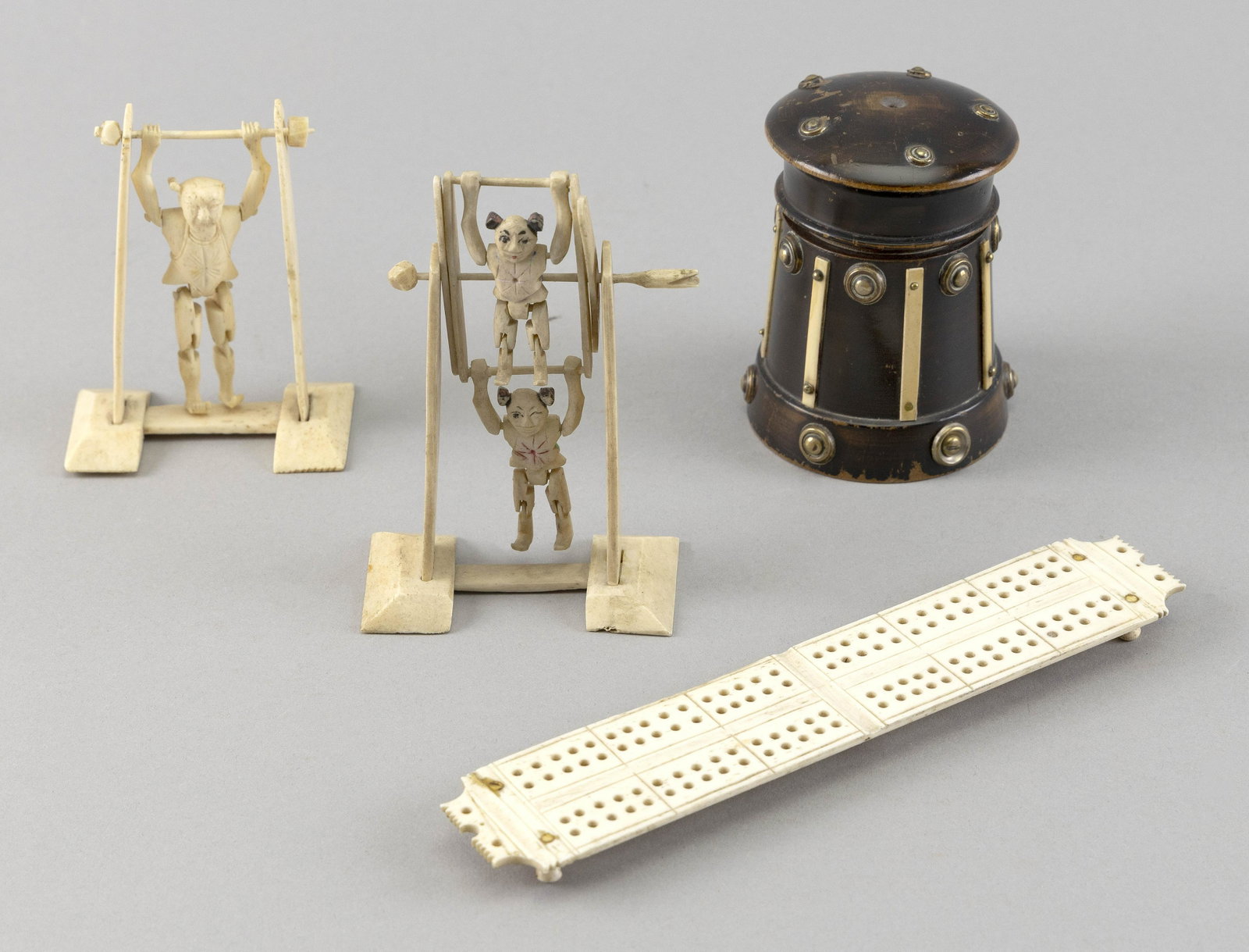 FOUR BONE ITEMS 19th/20th Century: FOUR BONE ITEMS 19th/20th Century A wooden sander with bone and metal appliques, height 3.25", a bone footed cribbage board, length 6.75", and two spinning acrobat figures, one with two poly