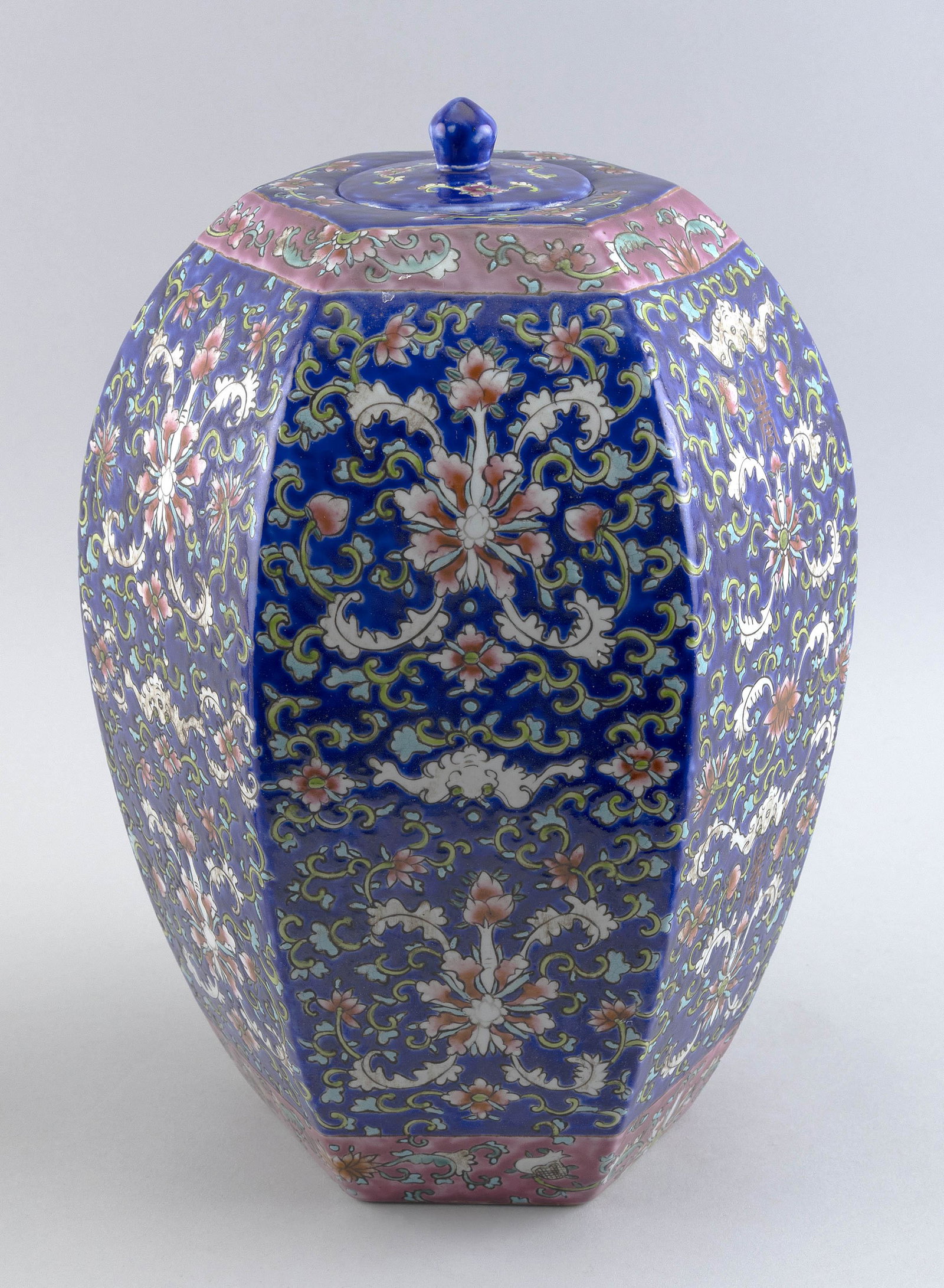CHINESE FAMILLE ROSE PORCELAIN HEXAGONAL COVERED JAR Early 20th Century Height 14".: CHINESE FAMILLE ROSE PORCELAIN HEXAGONAL COVERED JAR Early 20th Century Scrolling lotus and bat decoration against a blue ground with pink bands at shoulder and foot. Six-character Qianlong mark on ba