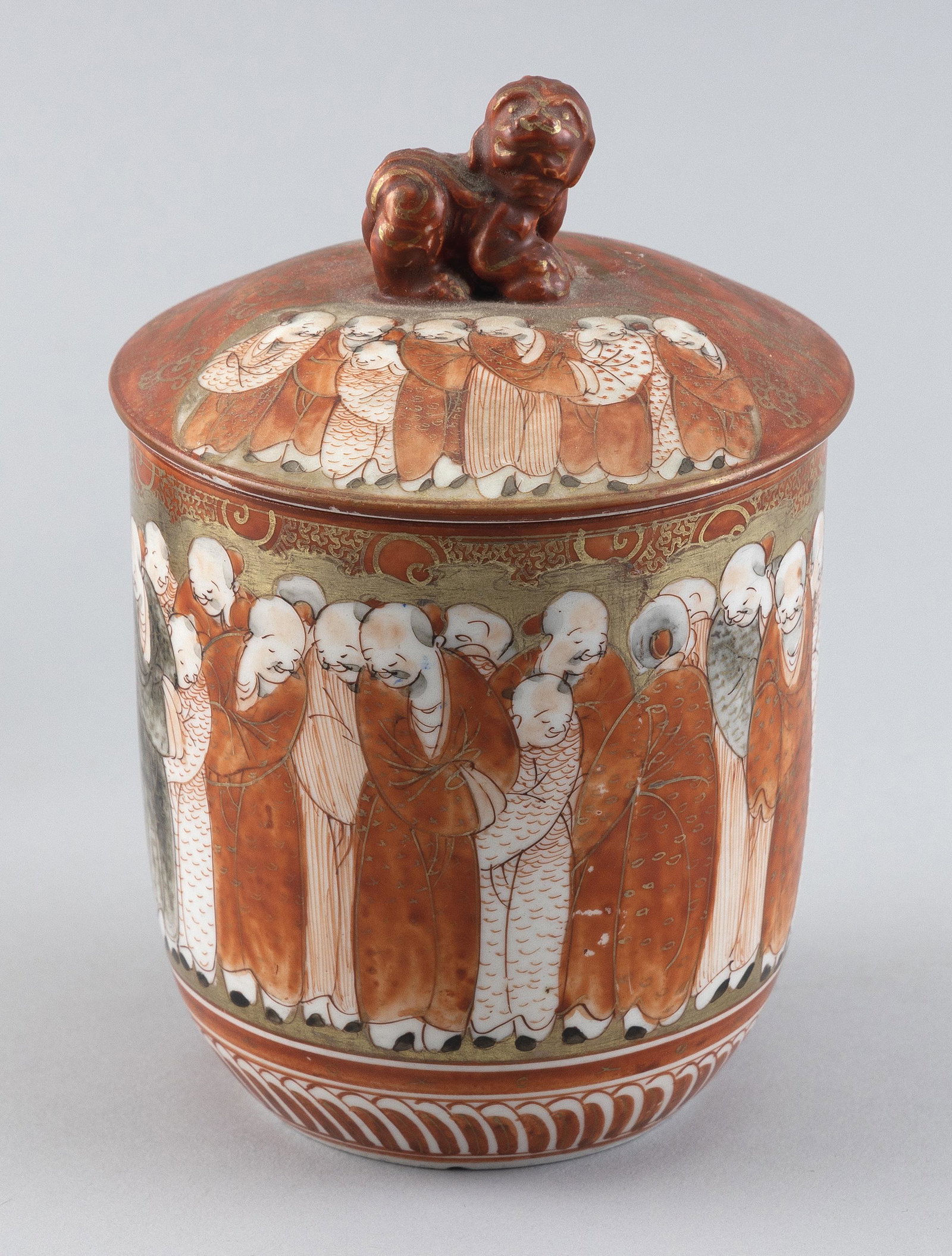 JAPANESE KUTANI PORCELAIN JAR Meiji Period Height 7".: JAPANESE KUTANI PORCELAIN JAR Meiji Period One Hundred Lohan decoration wraps around the cylindrical body. Cover with fu dog-form knop and continuation of the lohan decoration as well as gilt phoenix.