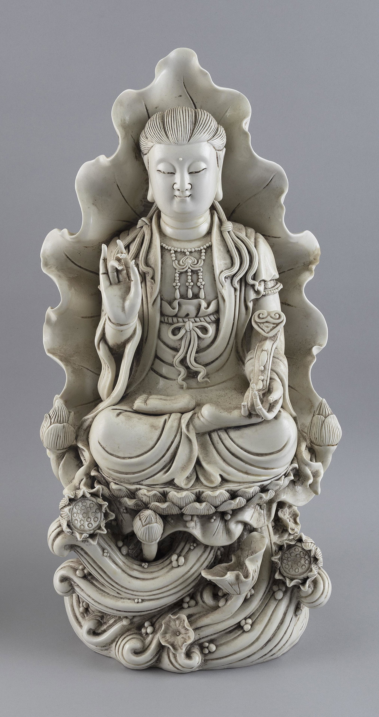 CHINESE BLANC DE CHINE PORCELAIN FIGURE OF GUANYIN Early 20th Century Height 20”.: CHINESE BLANC DE CHINE PORCELAIN FIGURE OF GUANYIN Early 20th Century Sitting on a wave base, holding a ruyi scepter in one hand and with her other hand in a teaching pose. Lotus-leaf mandorla and lot
