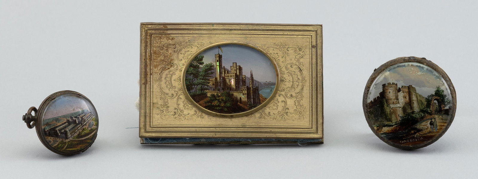 THREE ASSORTED PERSONAL ITEMS Last Quarter of the 19th Century Lengths from 1.25” to: THREE ASSORTED PERSONAL ITEMSLast Quarter of the 19th CenturyA watch-form pill box and two needle cases, each with painted landscape decoration.Lengths from 1.25” to 3.75”.