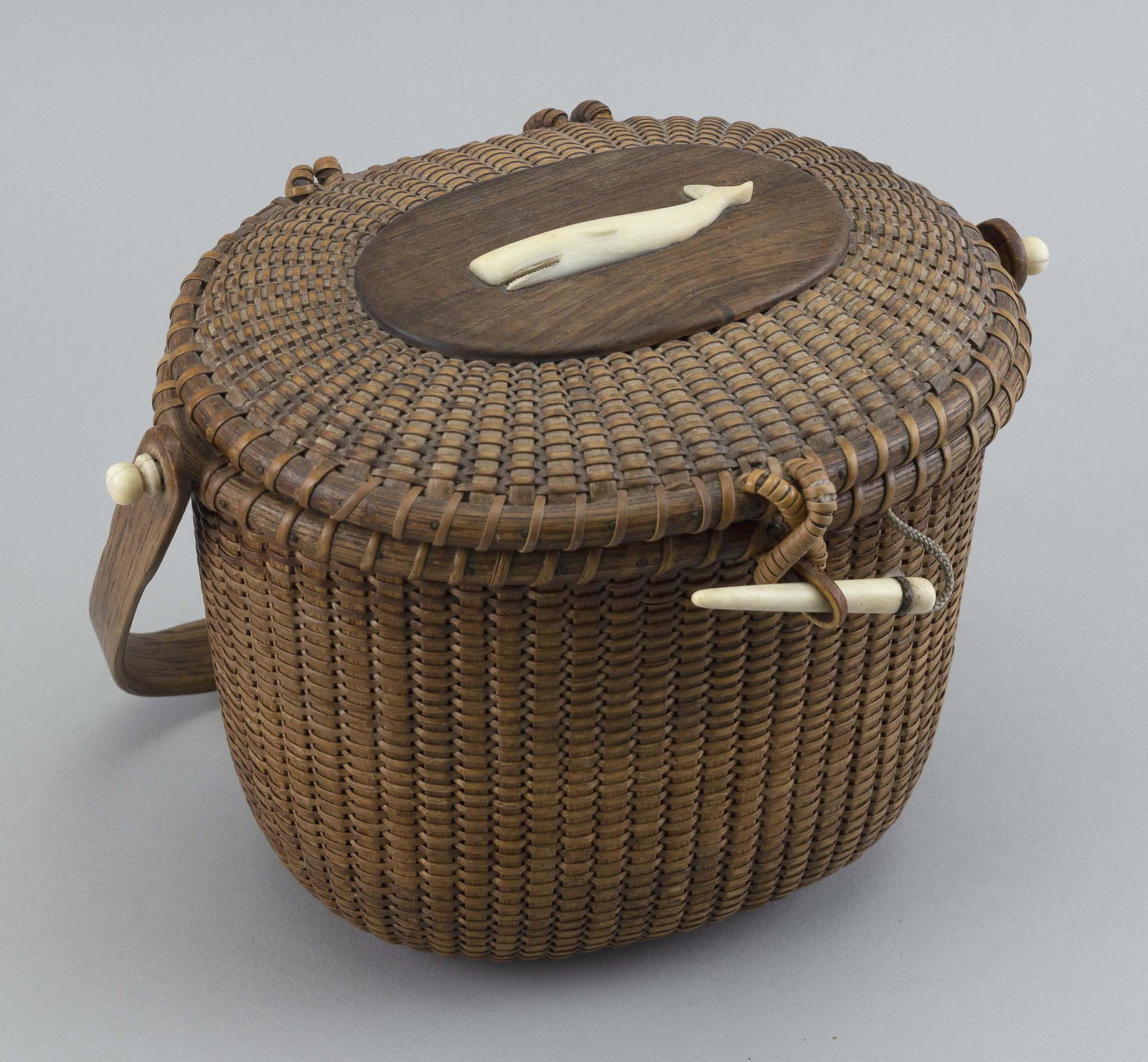 SHERWIN BOYER NANTUCKET BASKET PURSE Nantucket, Massachusetts, 20th Century Height 7”. Length: SHERWIN BOYER NANTUCKET BASKET PURSE Nantucket, Massachusetts, 20th Century Oval, with swing handle. Carved sperm whale plaque mounted to the top of the hinged lid. Owner's plaque mounted to inside of